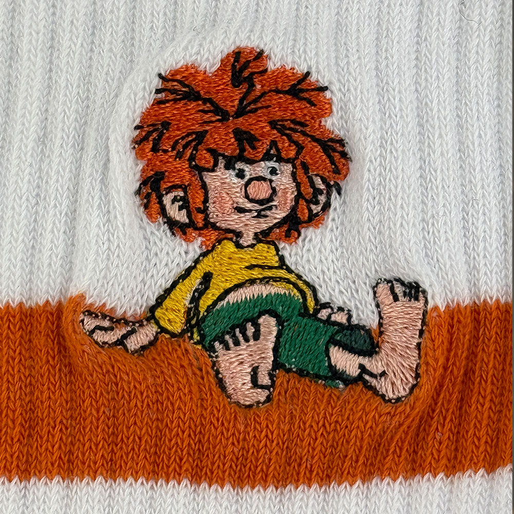 Bestickter Pumuckl auf weißen Tennissocken mit orangefarbener Borte, gestickte Figur lachend und sitzend.