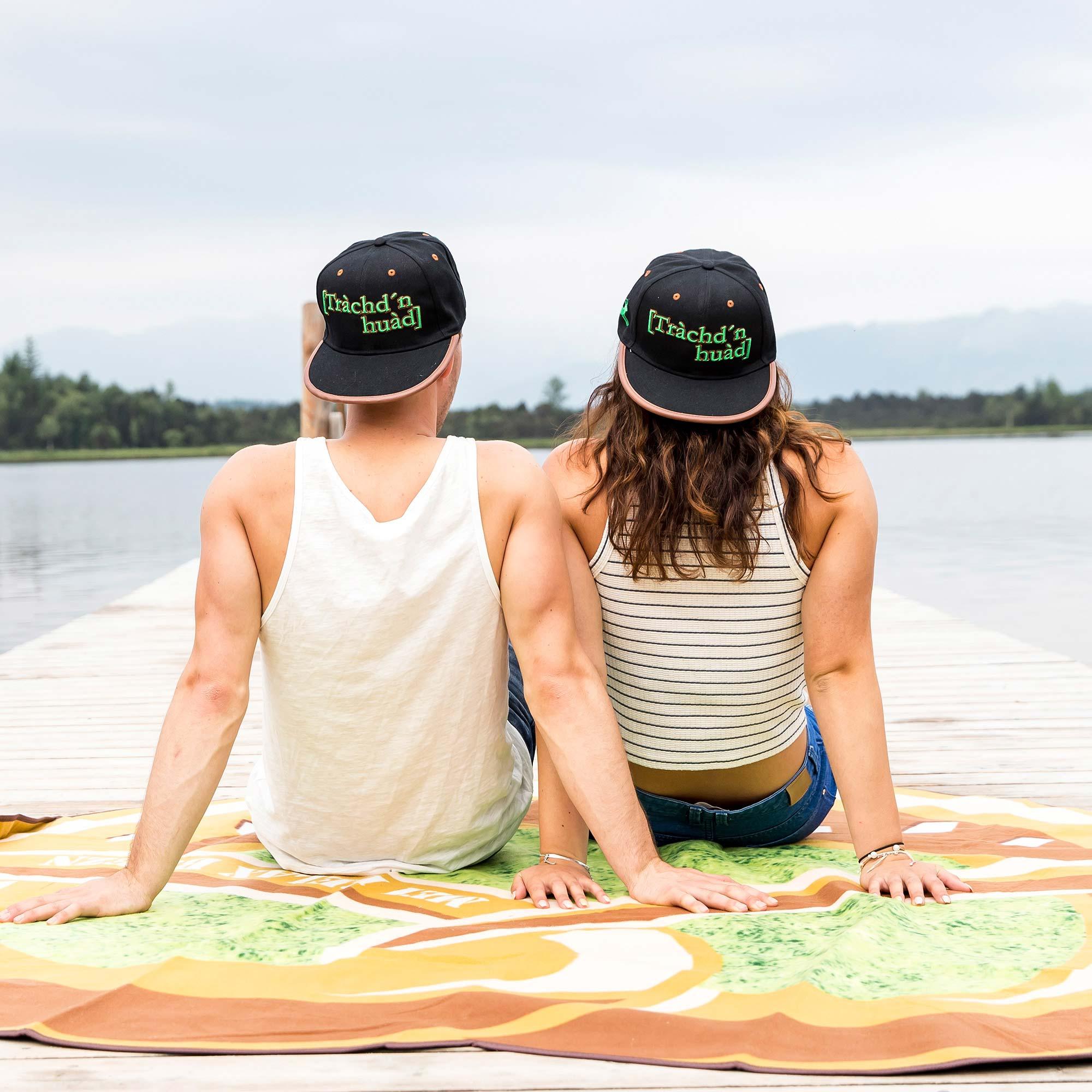 Graue Snapback Cap mit flachem Schirm, schwarzer Frontpanel, weißer Stickerei „Trachdnhuad“ in Schreibschrift.