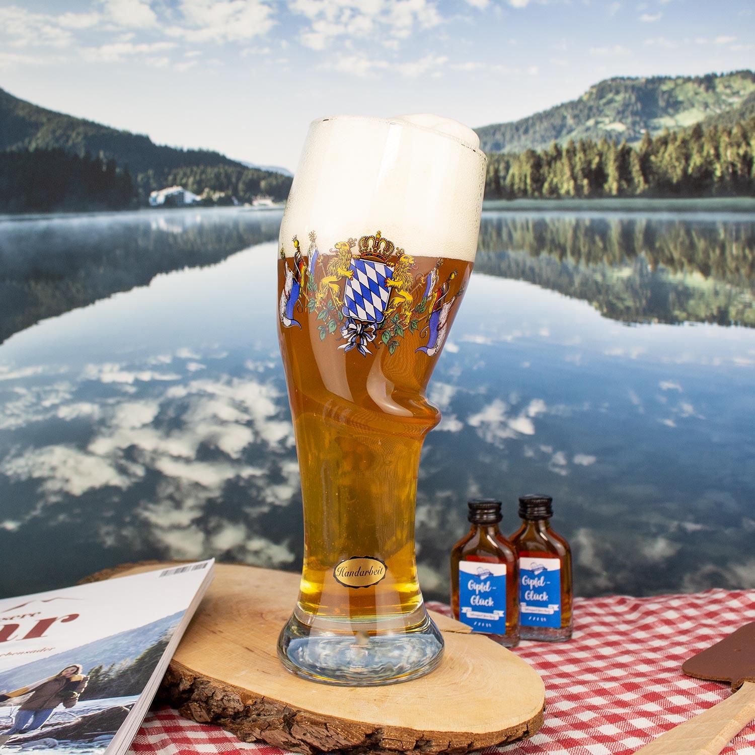 Originelles, bauchiges Bierglas mit bayerischem Wappen und Goldrand auf Holzscheibe vor Bergsee.
