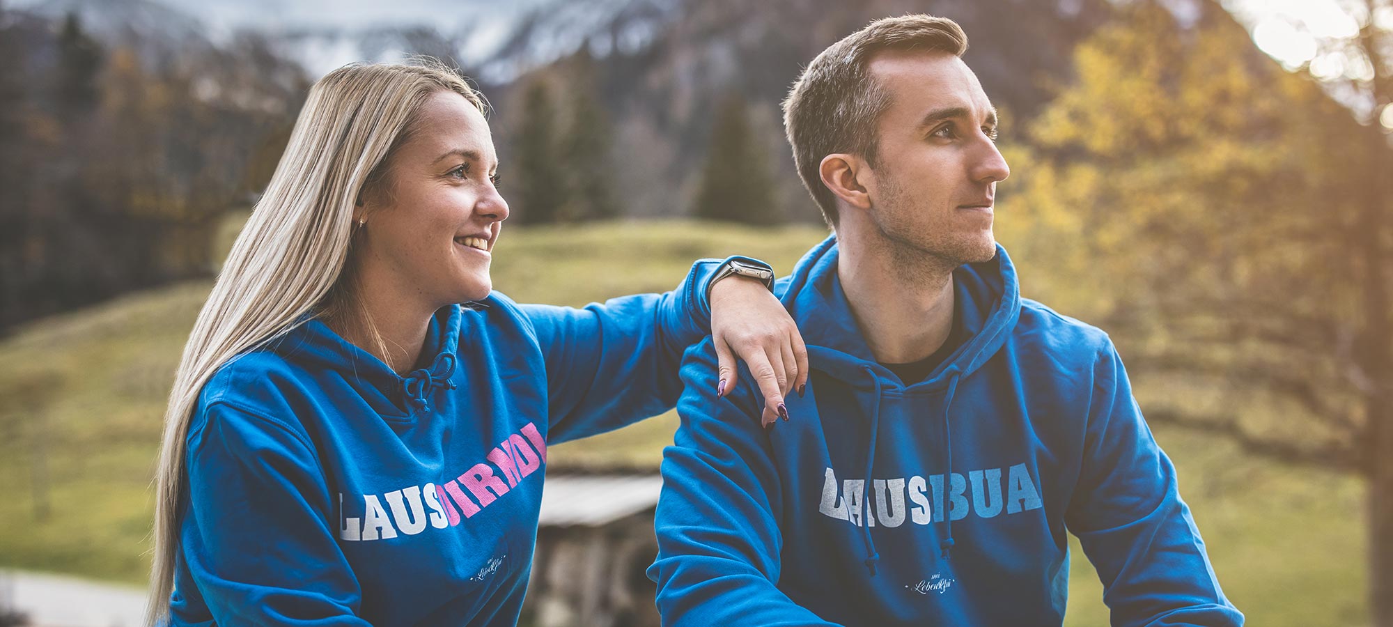 Fröhlicher junger Mann in schwarzem Kapuzenpullover und Hut zieht einen alten Leiterwagen, Kollektion für Buama.