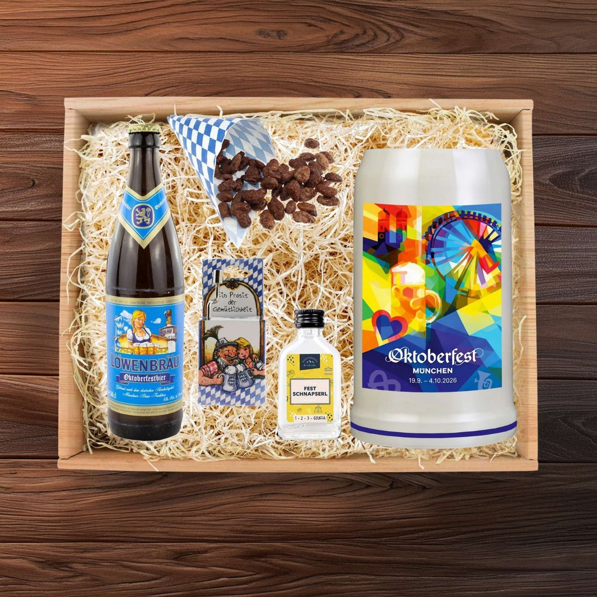 Oktoberfest Geschenkbox mit Löwenbräu Bier, Keramikkrug, gebrannten Mandeln und Schnapsfläschchen auf Holzwolle.