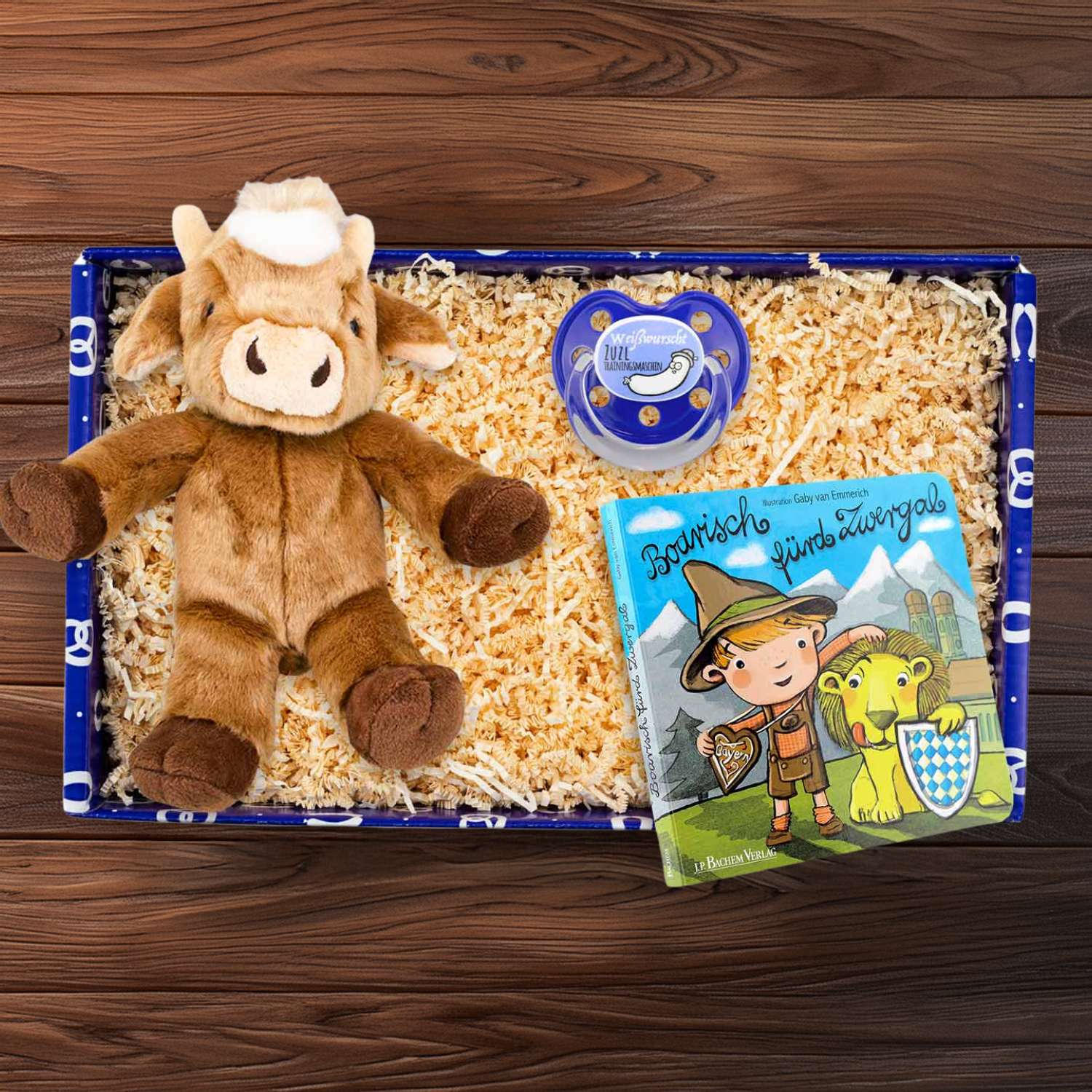 Bayerische Baby-Geschenkbox mit Plüsch-Kuh, Holz-Zuzlmaschine und Buch „Boarisch fürd Zwergal“, Farben: Blau, Beige.