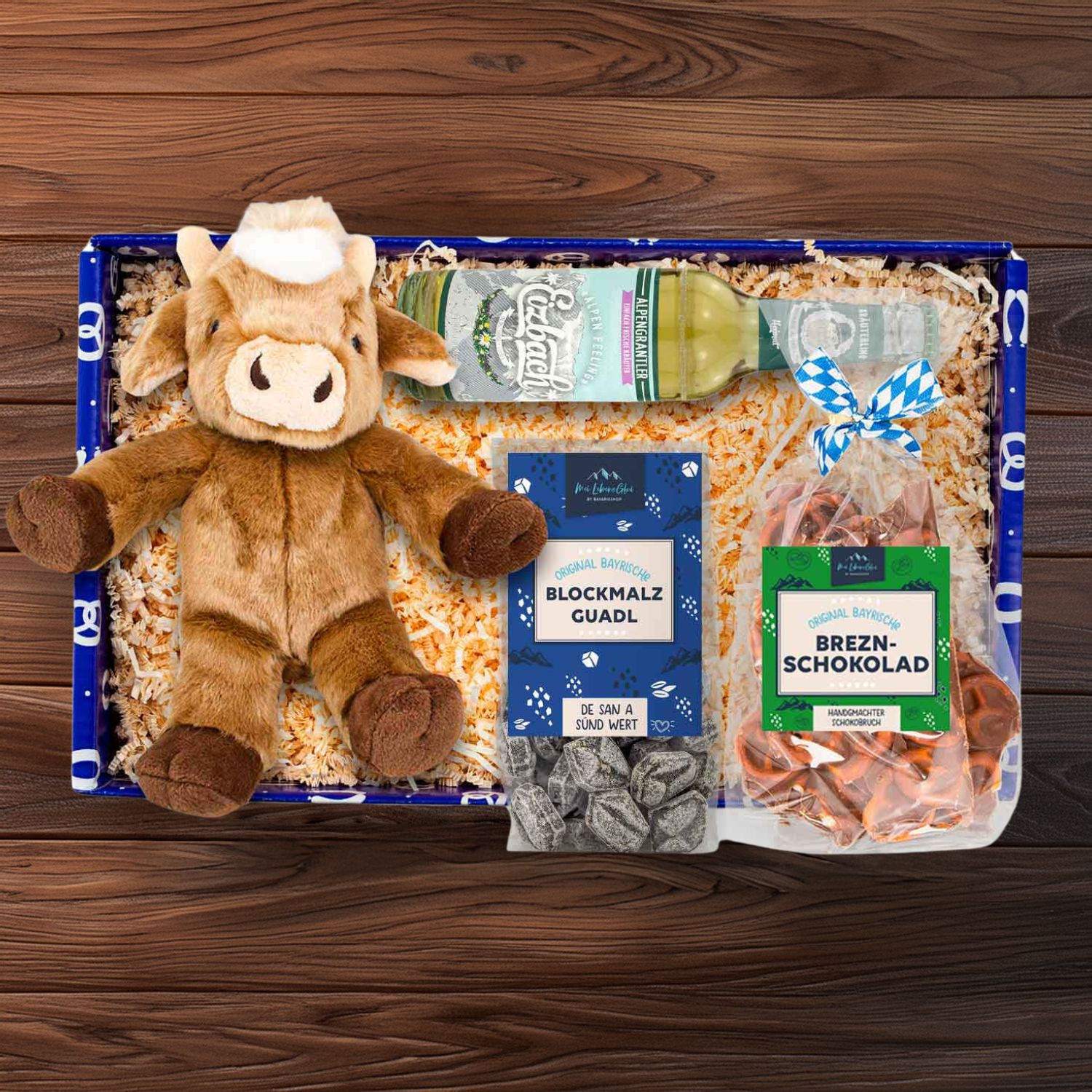 Geschenkbox mit Plüsch-Kuh, Brezn-Bruch-Schokolade, Kräuter-Limo und weiteren bayerischen Spezialitäten.