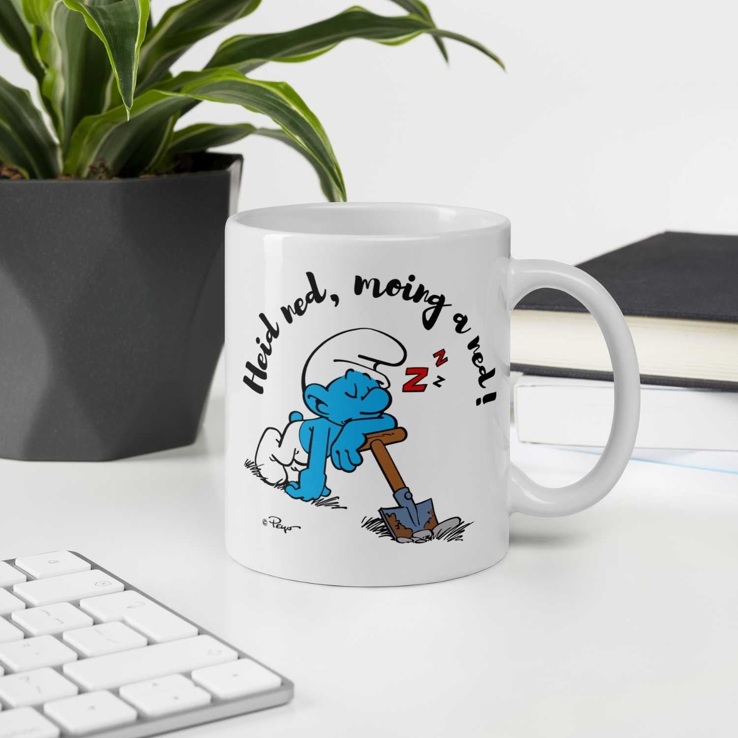 Weiße Porzellan-Tasse mit bedrucktem Schlumpf-Motiv und bayerischem Schriftzug „Heid ned, moing a ned“, 330 ml.