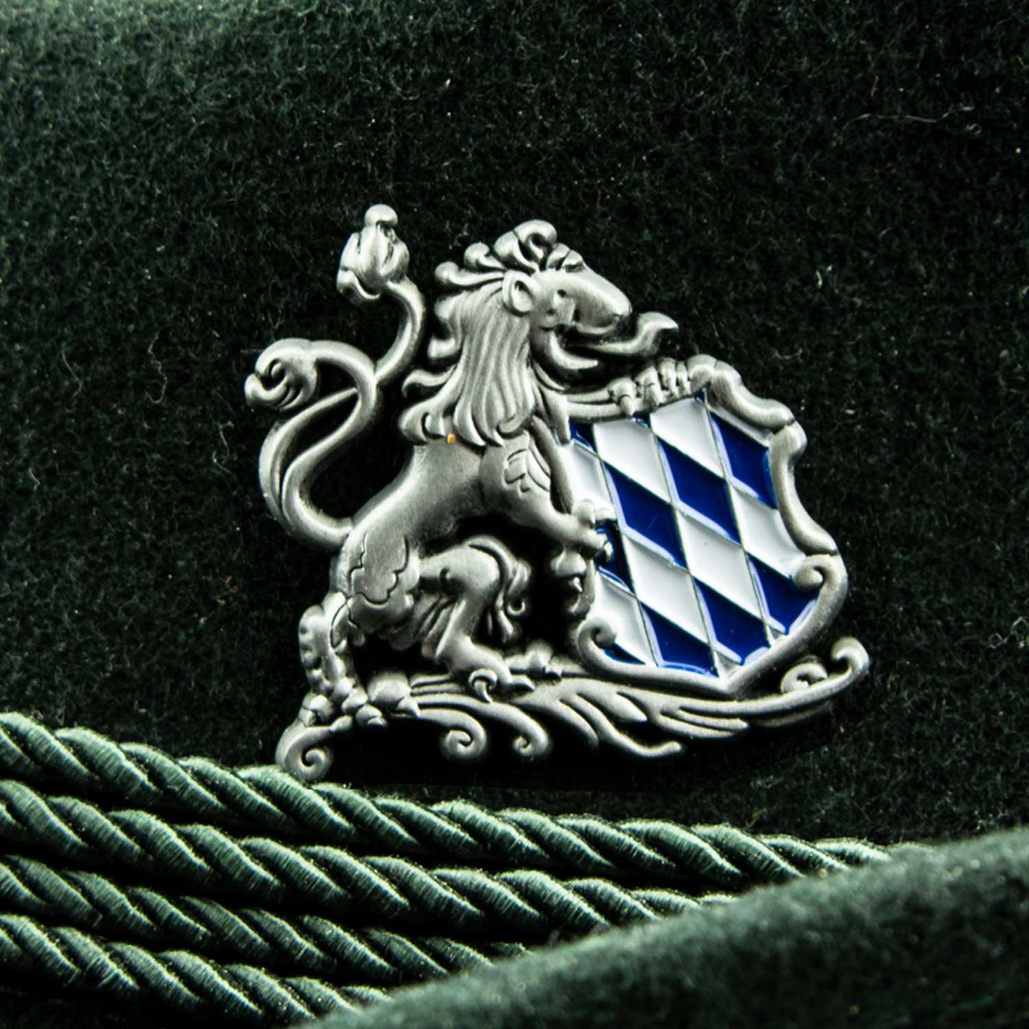 Silberfarbener Ansteck-Pin mit Löwenmotiv und weiß-blauem Rautenmuster, mit Schmetterlingsverschluss, ca. 4 × 3,7 cm.