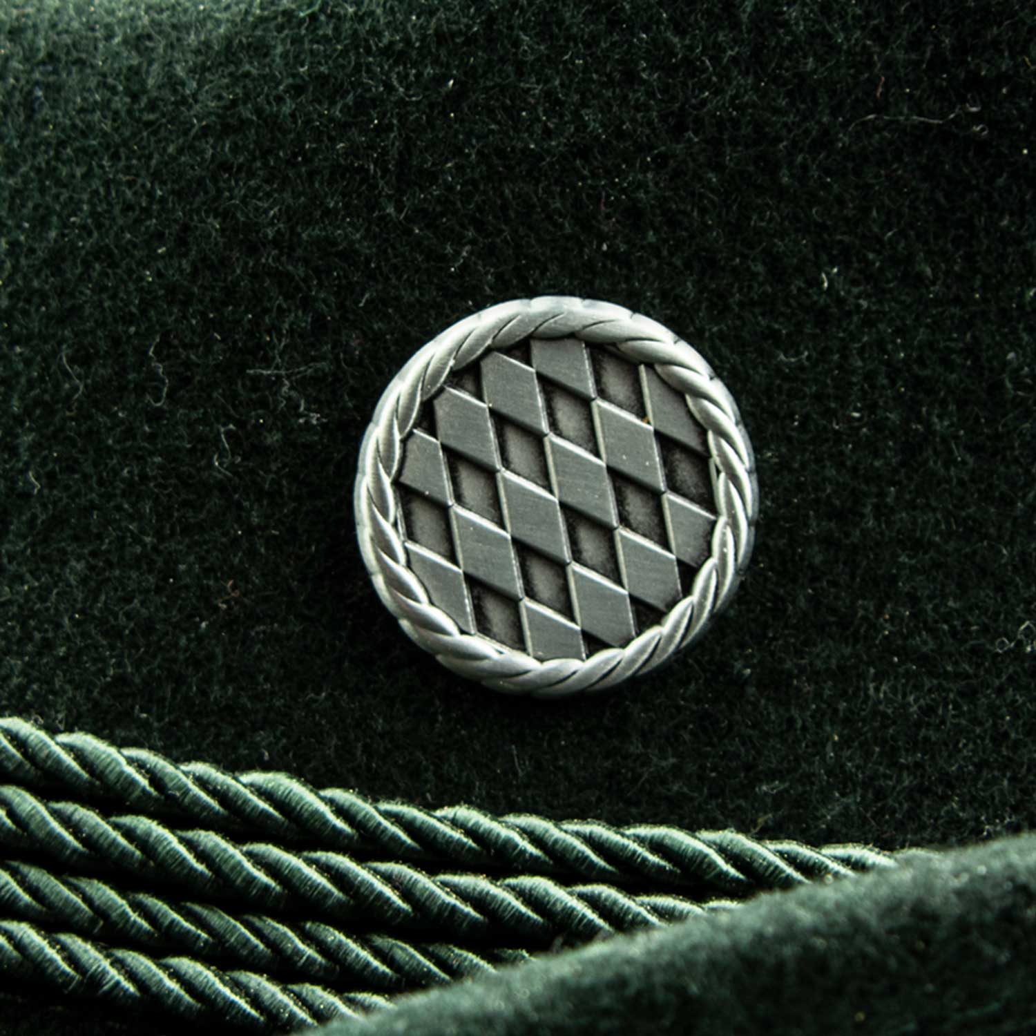 Runder, silberfarbener Pin mit bayerischem Rautenmuster und Kranz, Schmetterlingsverschluss auf der Rückseite.