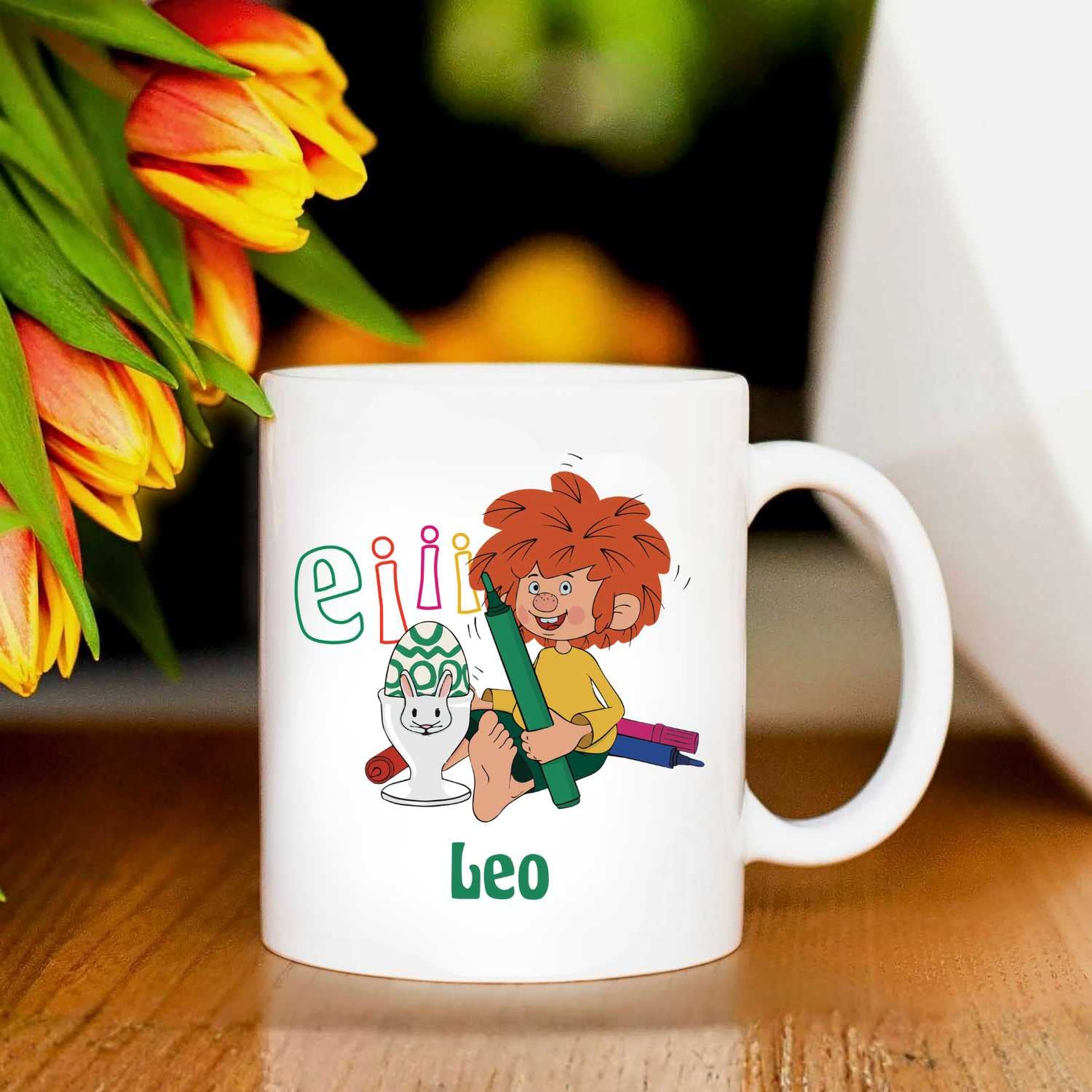 Weiße Keramiktasse mit Pumuckl-Motiv, Schriftzug Eiii, Osterei und bunten Tulpen im Hintergrund.