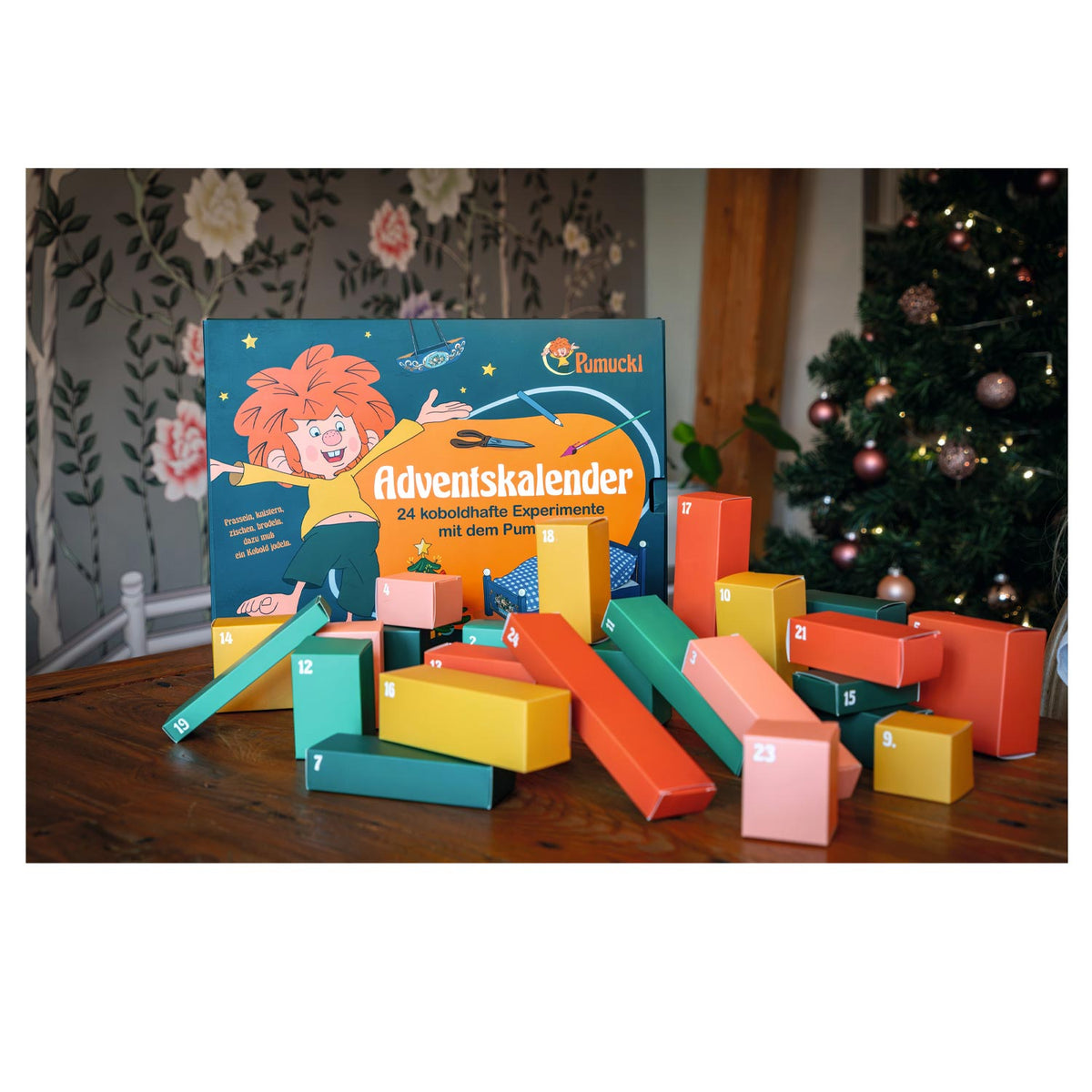 Geöffneter Pumuckl Adventskalender: 24 bunte Pappboxen vor dem Christbaum