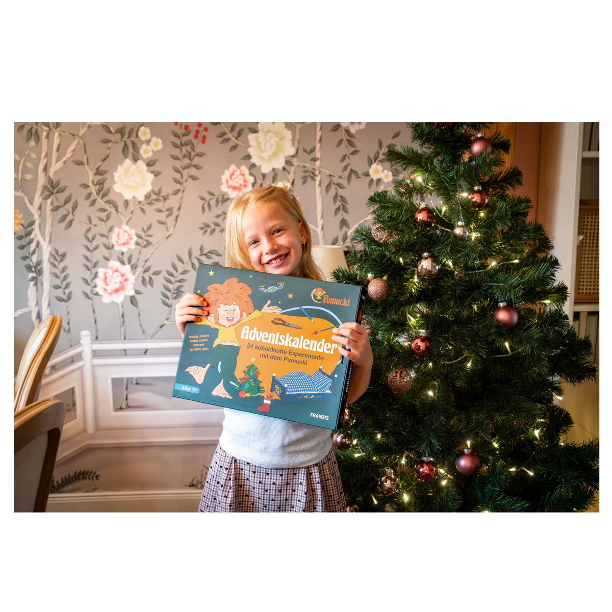 Mädchen hält den Pumuckl Adventskalender vor dem Weihnachtsbaum
