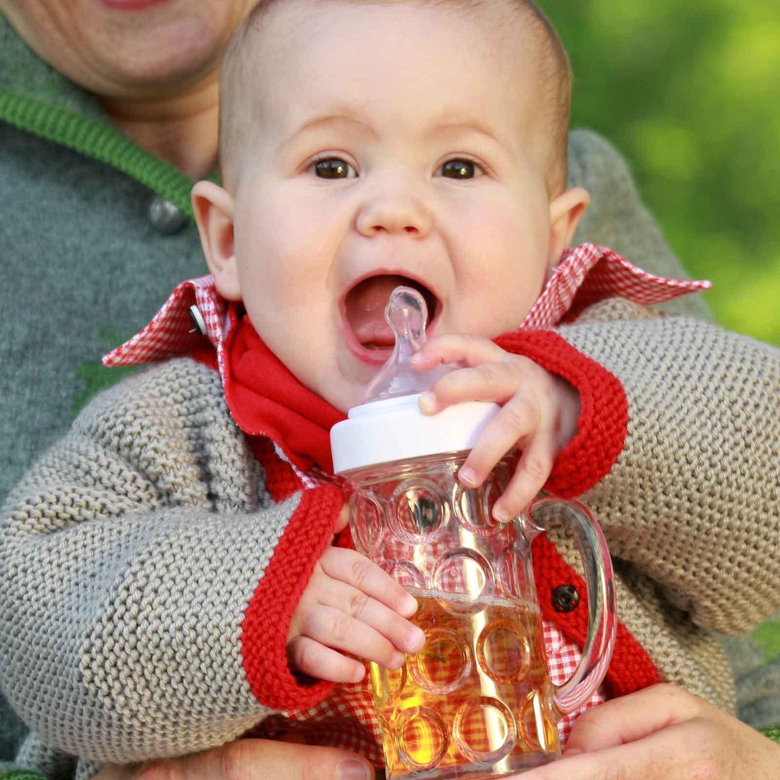 Fröhliches Baby in beige-roter Strickjacke trinkt aus einem originellen Seidel-Babyfläschchen mit transparentem Design.