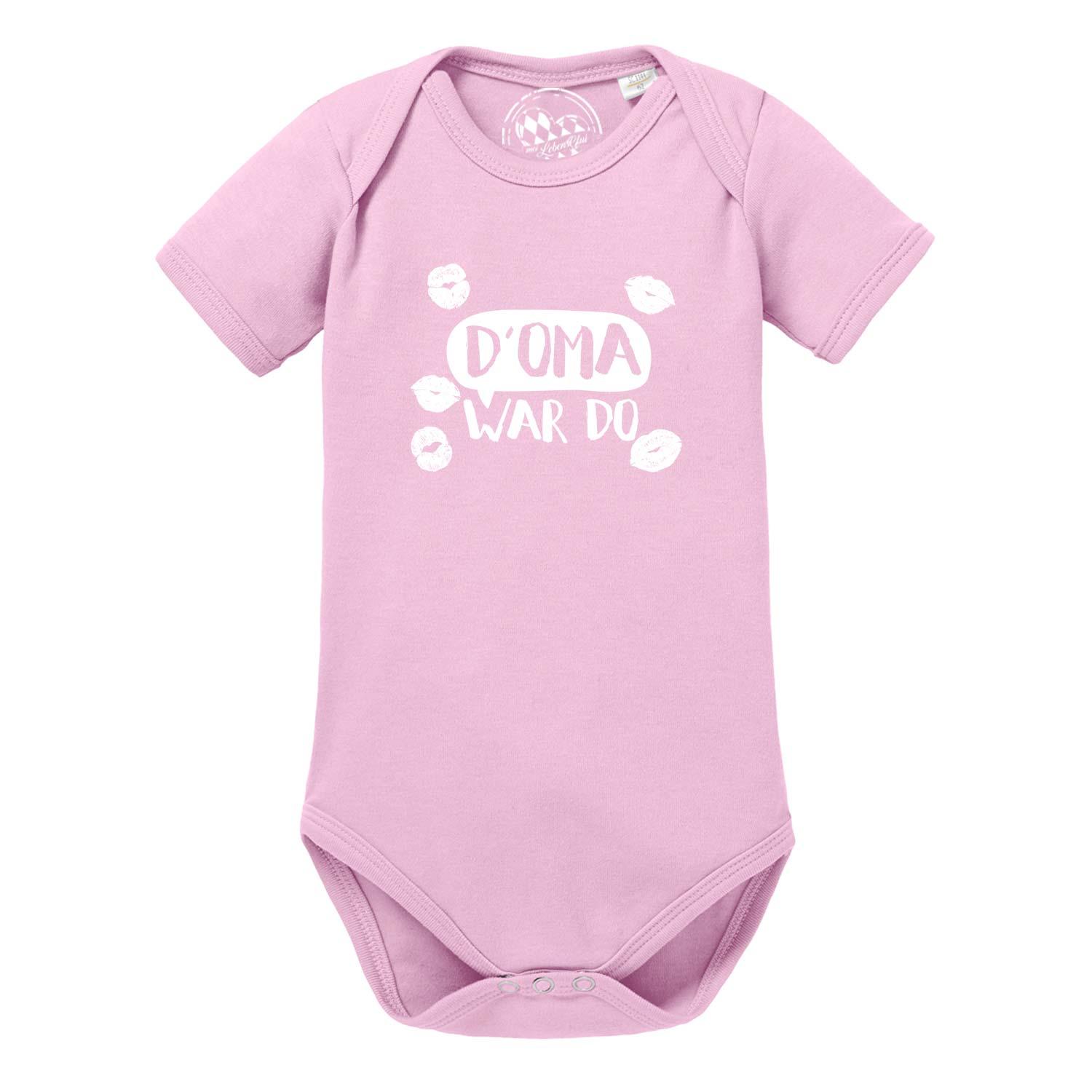 Weißer Babybody mit kurzen Ärmeln, grauem Schriftzug „D’ Oma war do…“ und Herz-Motiv auf der Brust; aus Baumwolle.