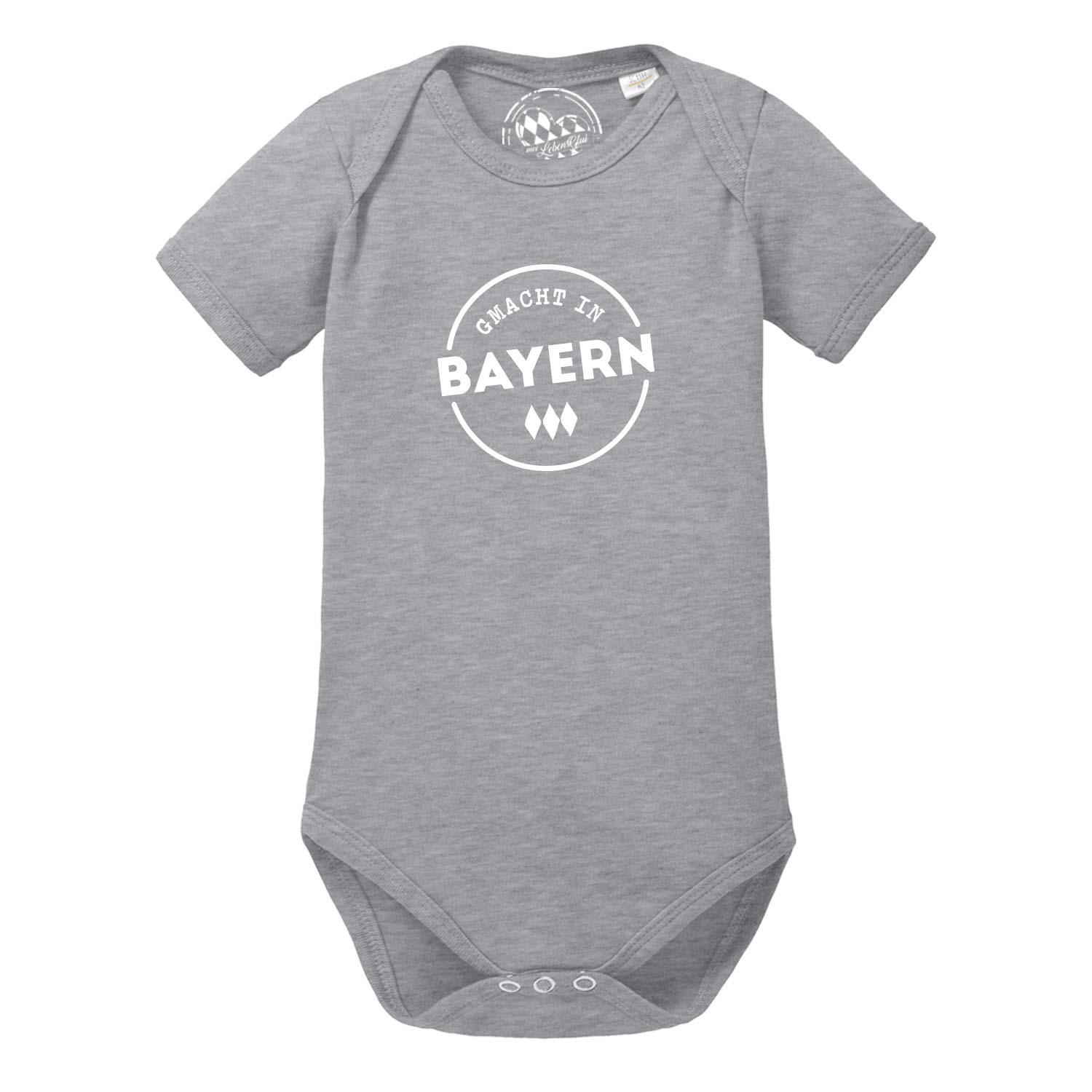 Kurzarm-Babybody in Weiß mit blauem Herz-Motiv und Aufschrift „gmacht in Bayern“, aus weicher Baumwolle.