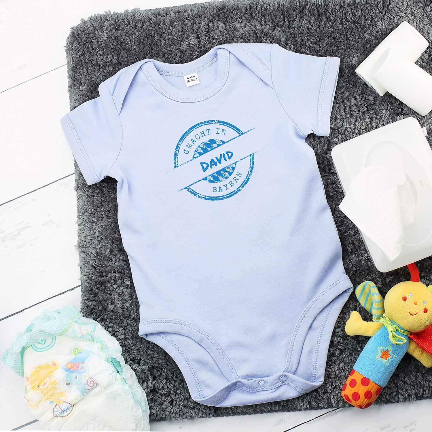 Blauer Baby Body mit kurzem Arm, Aufdruck "gmacht in Bayern" und Wunschnamen, Druckknöpfe im Schritt, Baumwolle.