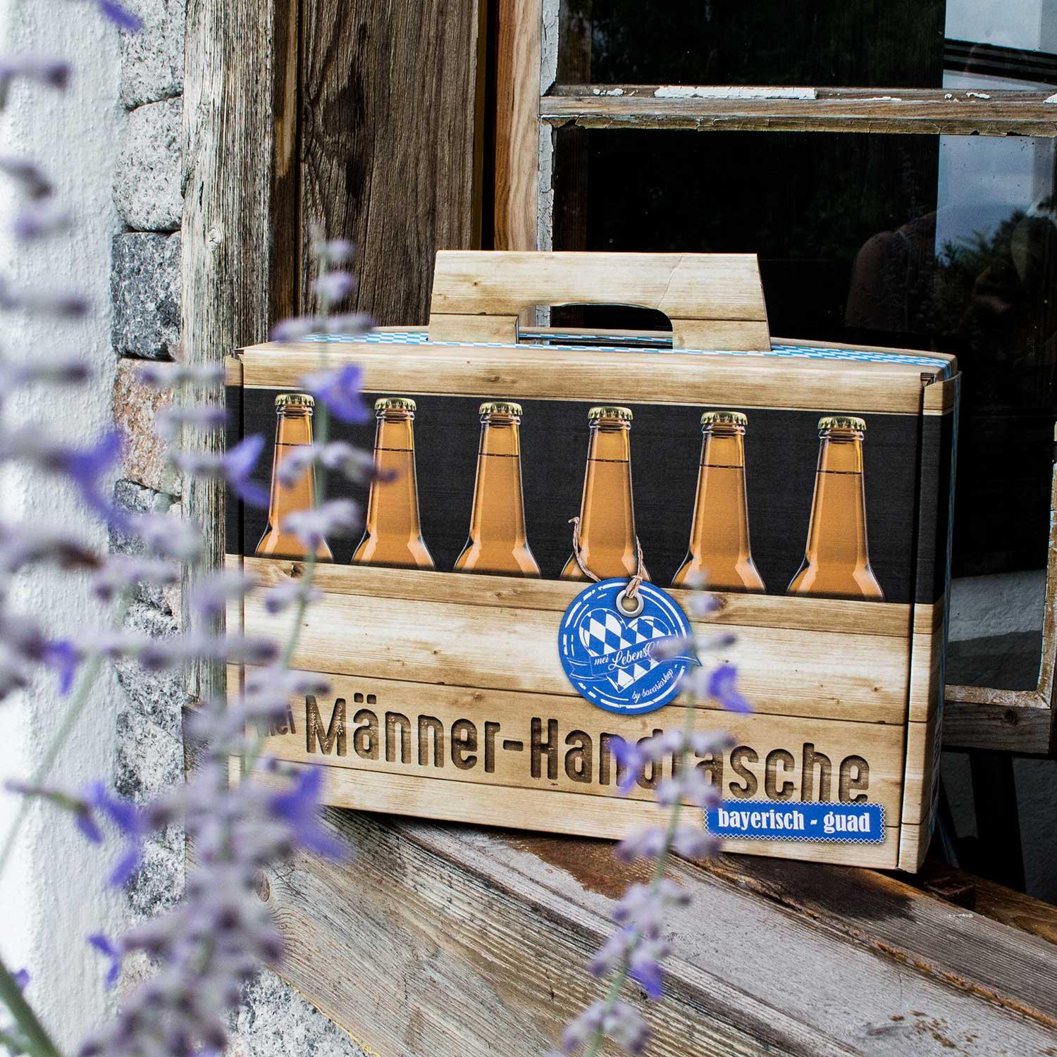 Holzoptik Bier-Geschenk "Männer-Handtasche" mit bayerischem Rautenmuster vor rustikaler Holzwand und Lavendel.