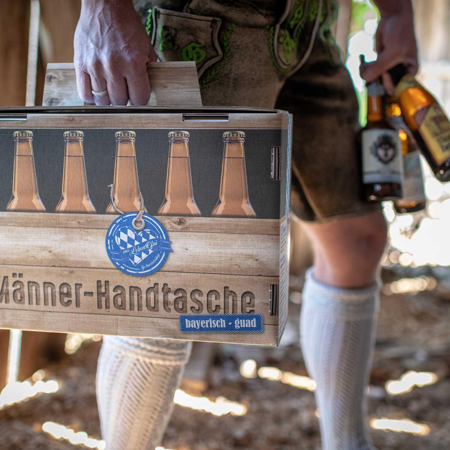 Mann in Lederhose trägt Bier-Geschenk Männer-Handtasche mit bayerischem Spruch und Bierflaschen.