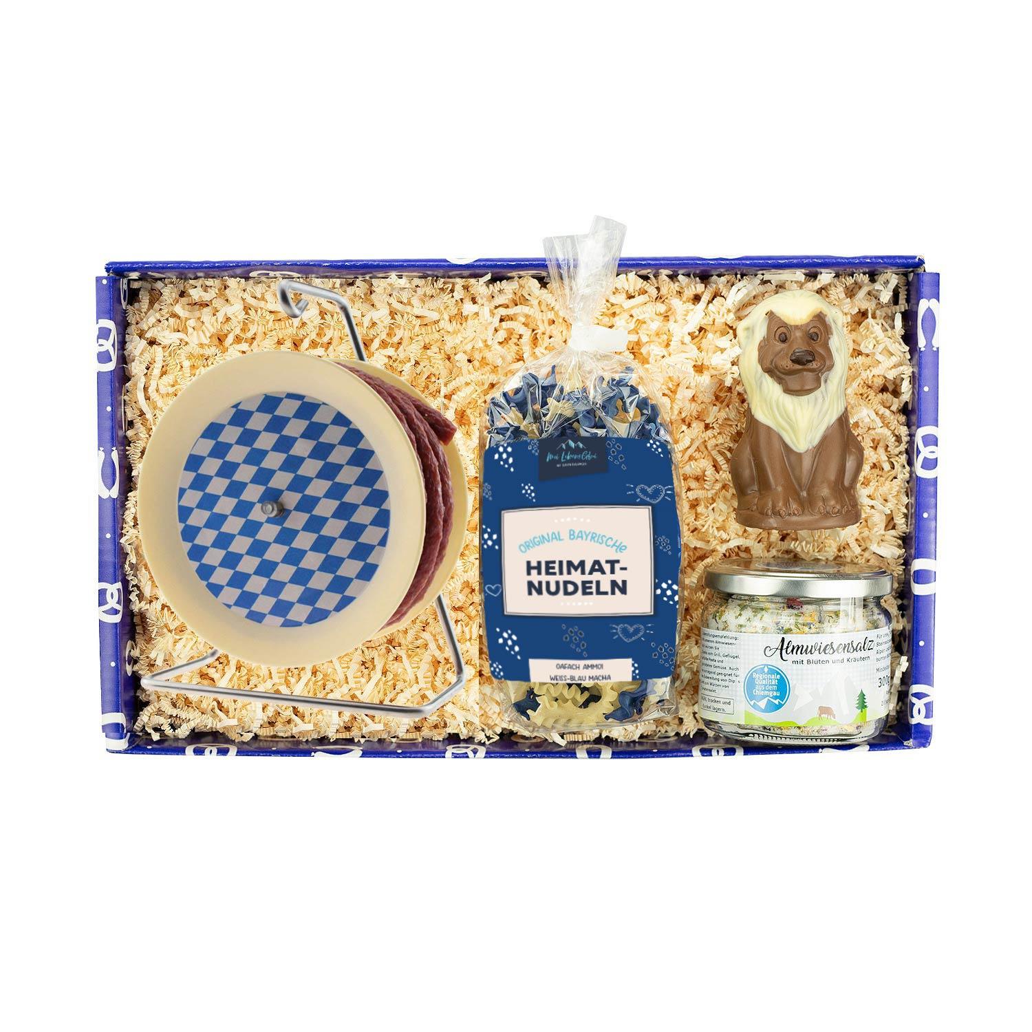 Geschenkbox mit bayerischer Salami auf Kabeltrommel, weiß-blauen Nudeln und Almwiesensalz mit Blüten.