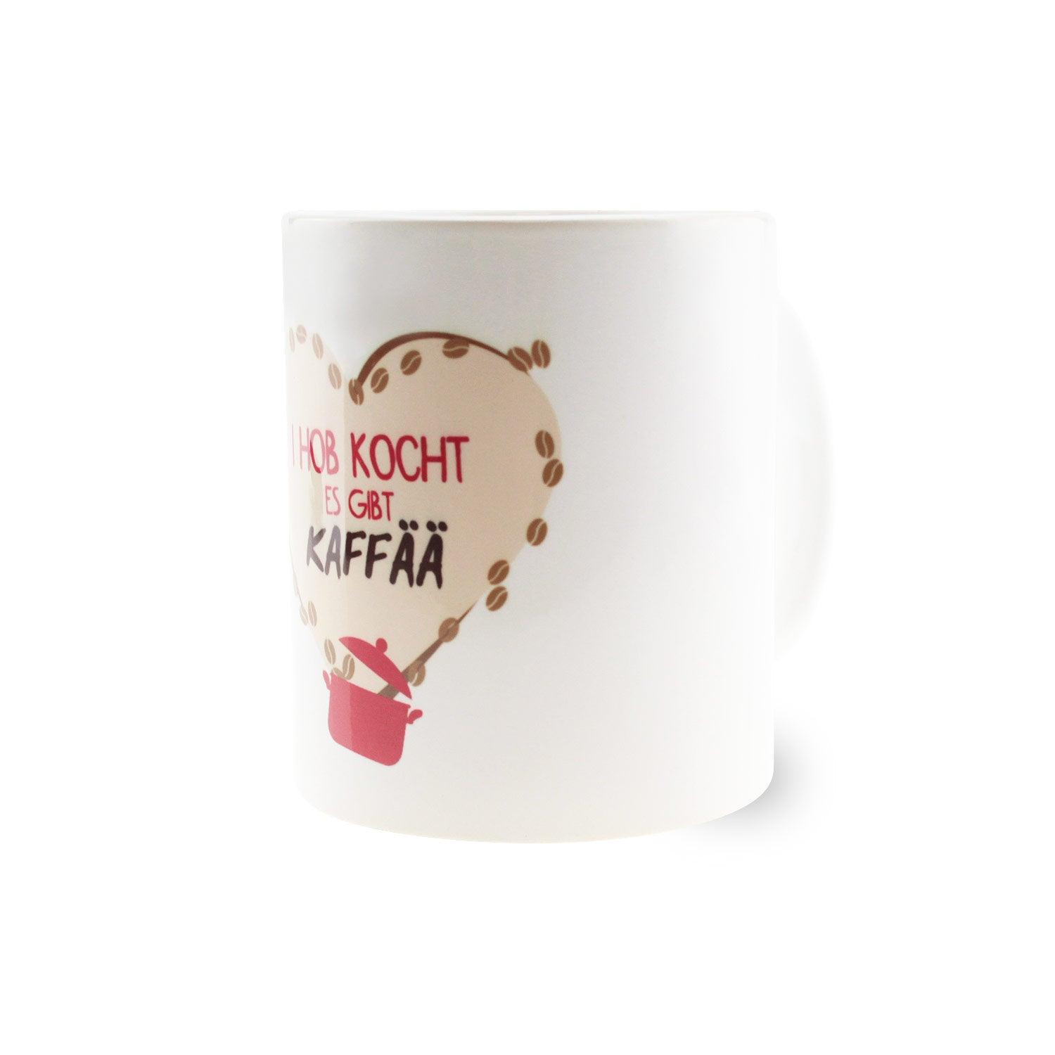 Weiße Keramiktasse mit schwarzem Henkel und Aufdruck „I hob kocht – es gibt Kaffää“, Fassungsvermögen 330 ml.