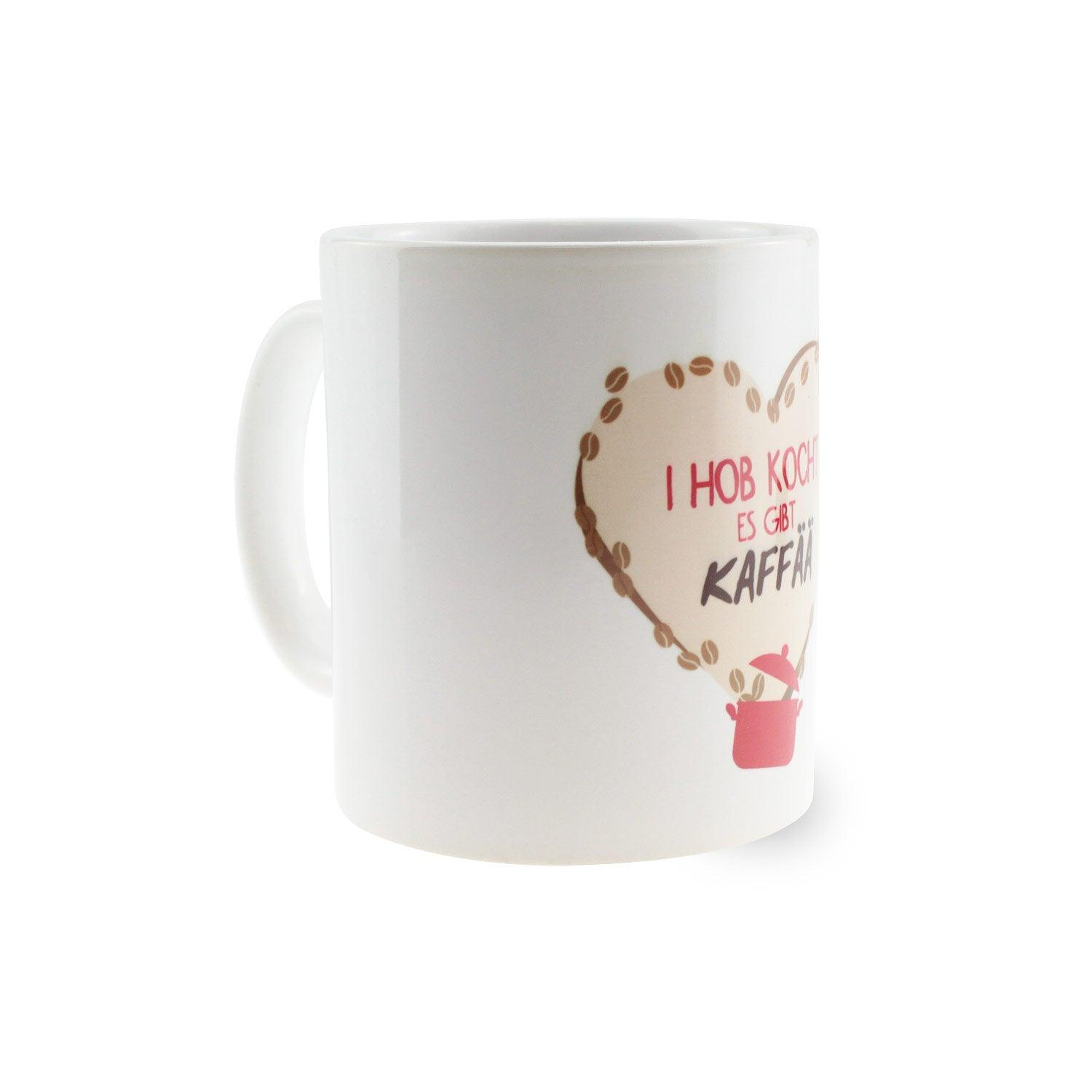 Weiße Kaffeetasse mit schwarzem Henkel und schwarzem Boden, Aufdruck „I hob kocht – es gibt Kaffää“, ca. 330 ml.