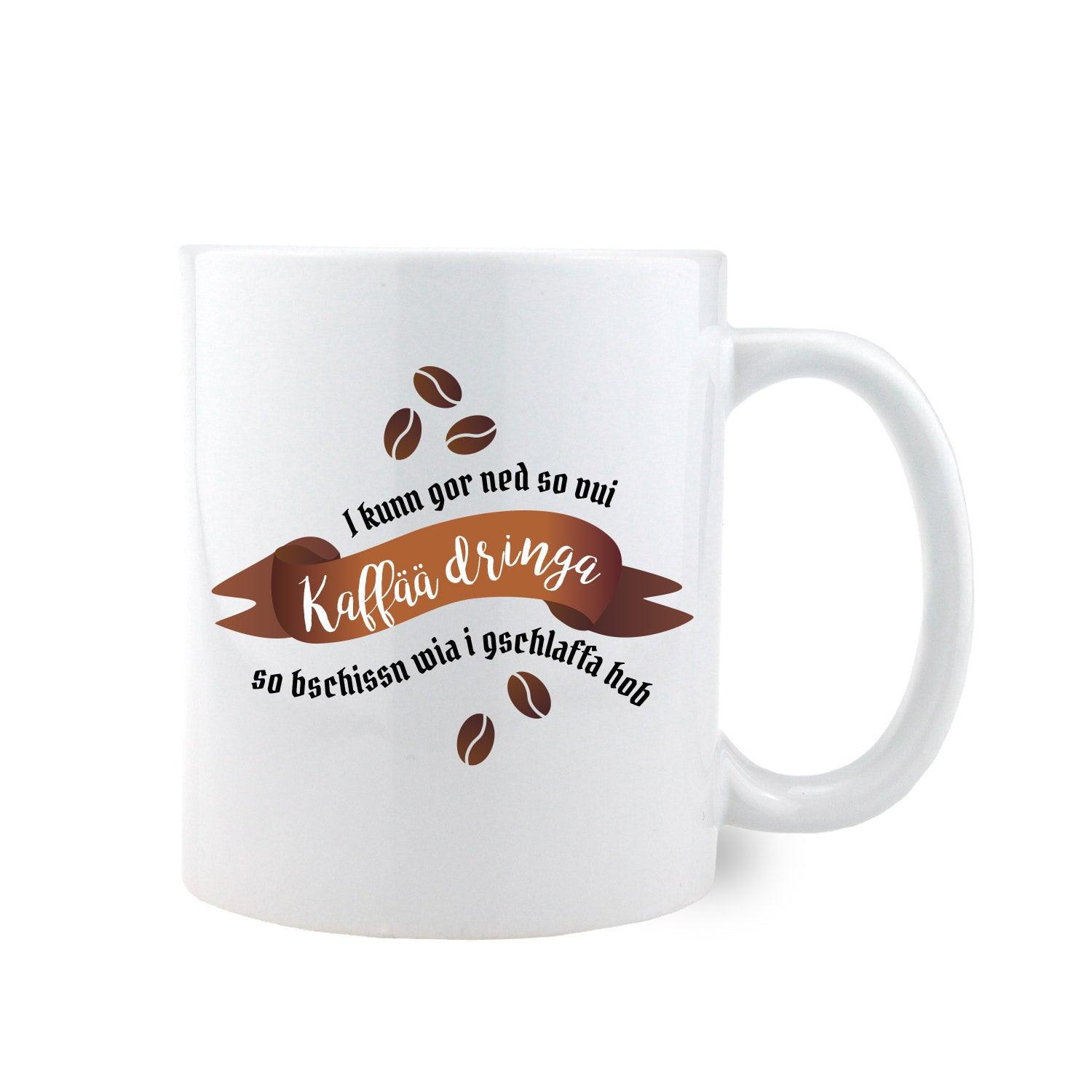 Weiße Keramiktasse mit schwarzem Henkel und Spruch „I kunn gor ned so vui Kaffää dringa...“, ca. 330 ml, ca. 9,5 cm hoch.