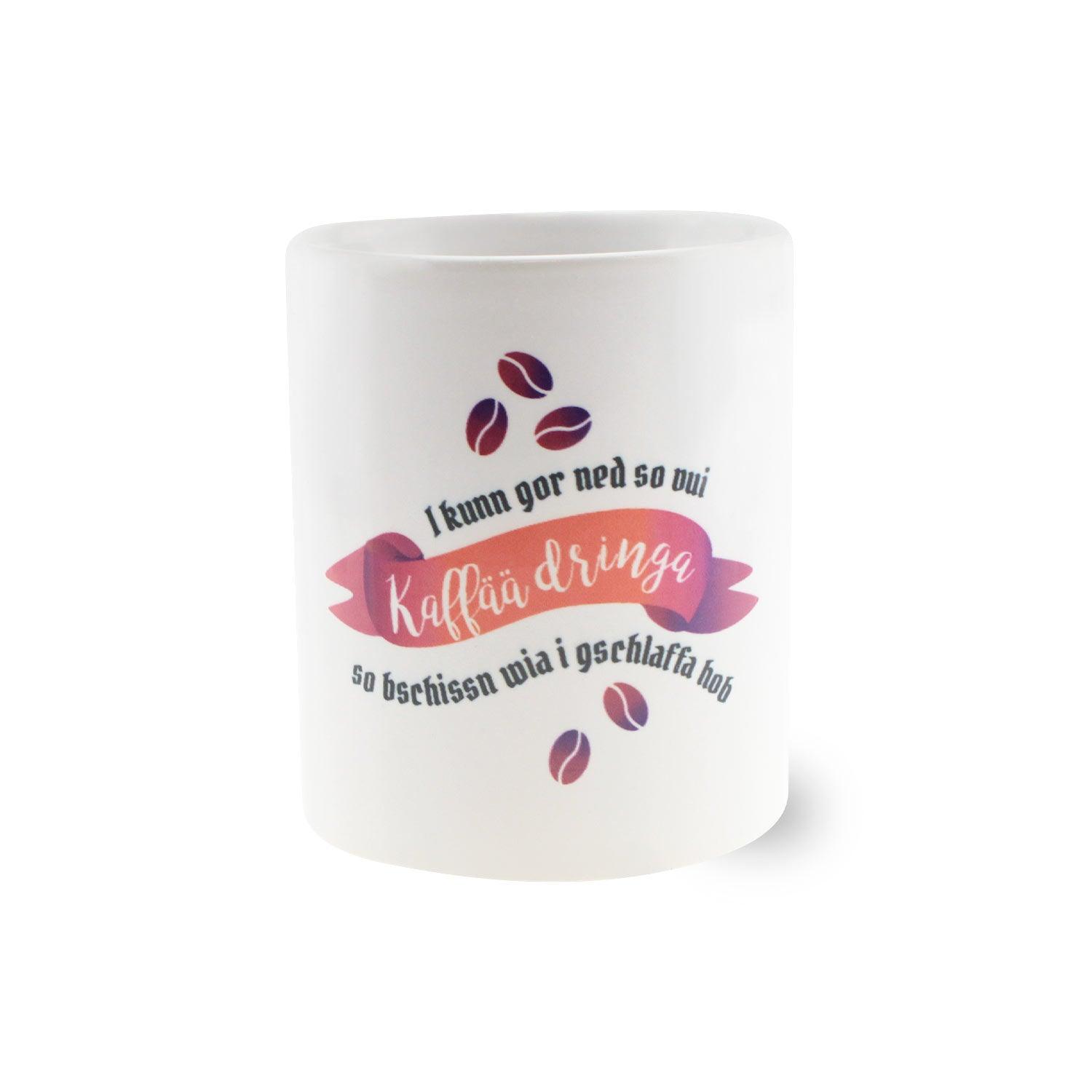 Weiße Keramiktasse mit schwarzem Henkel und Bayernspruch „I kunn gor ned so vui Kaffää dringa…“, ca. 330 ml, 9,5 cm hoch.