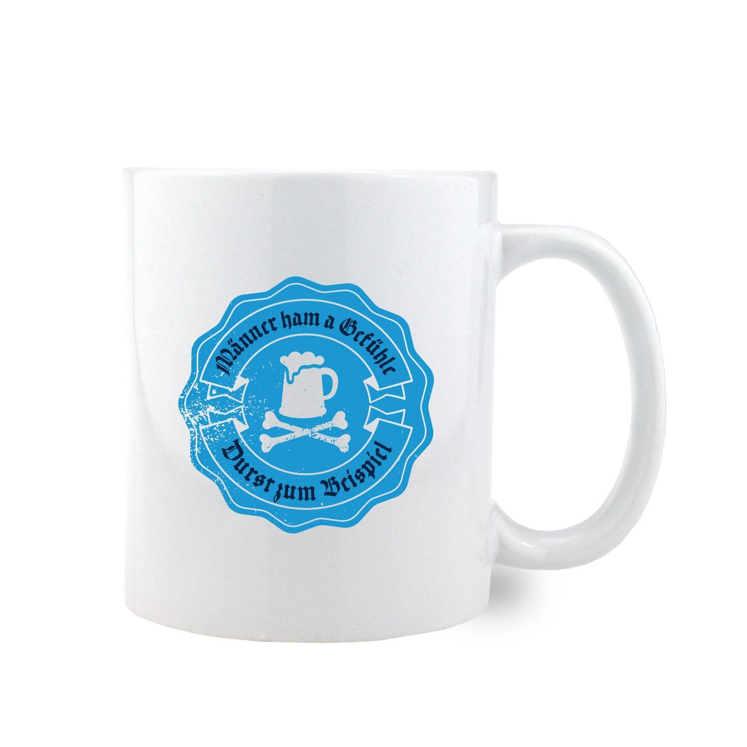 Weiße Keramiktasse mit schwarzem Henkel und schwarzem Innenbereich, bedruckt mit dem Spruch „Männer ham a Gefühle – Durst zum Beispiel“.