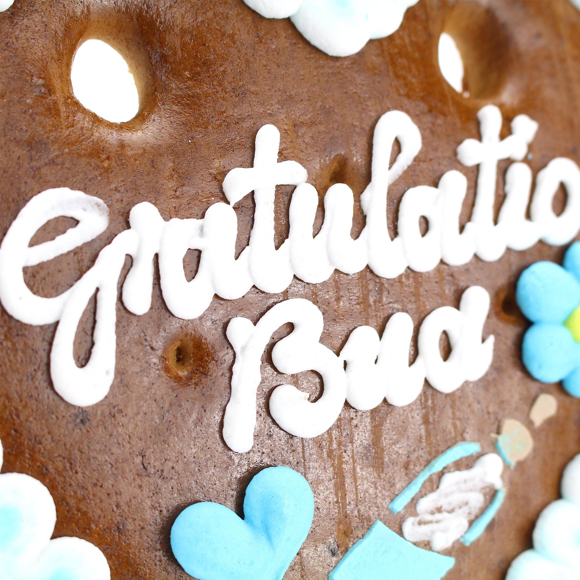 Herzförmiges Lebkuchenherz mit weiß-blauem Zuckerrand und Aufschrift „Gratulation Bua“, handgefertigt, 14 × 17 cm.