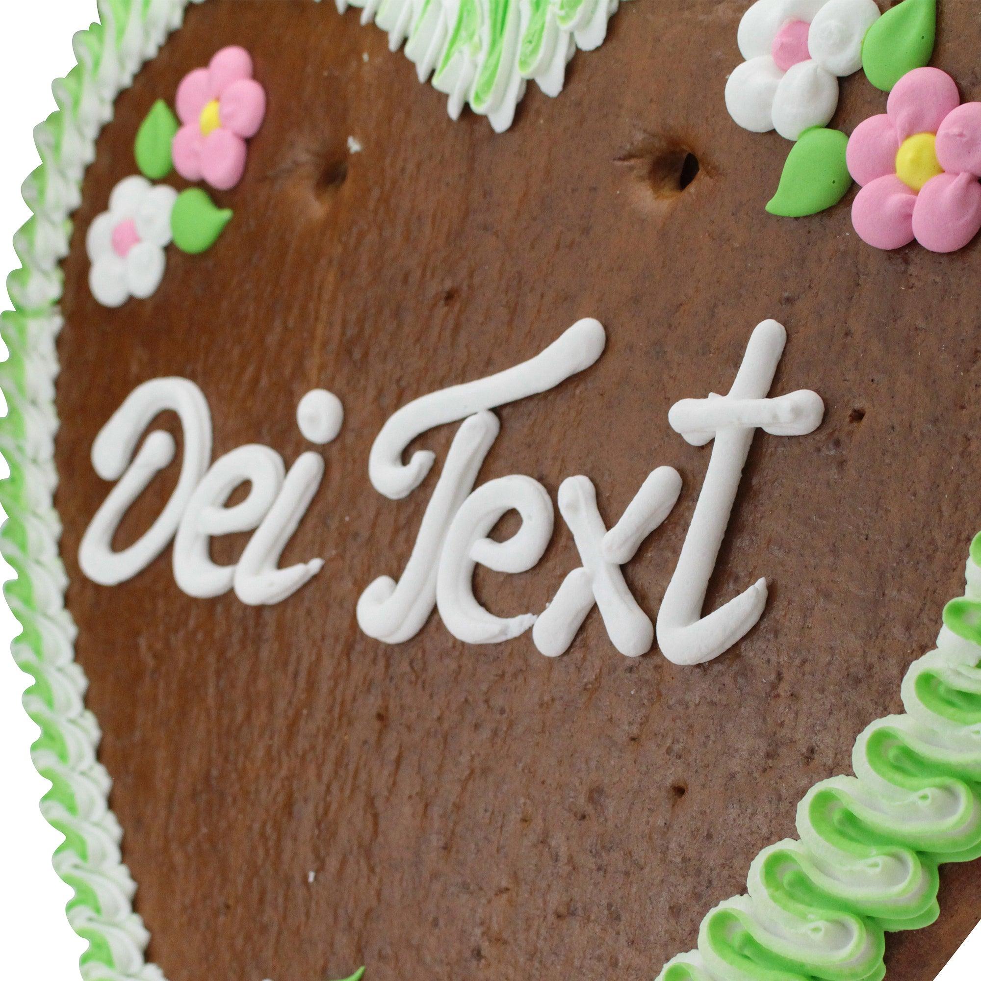 Großes, herzförmiges Lebkuchenherz mit weißer Zuckerschrift, bunten Zuckerblumen und Randverzierung, ca. 48×50 cm.