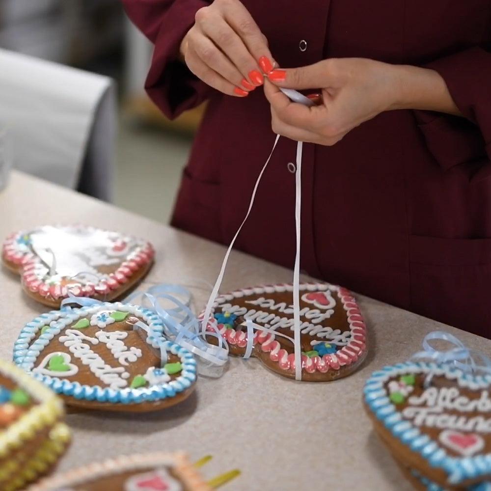 Kleines braunes Lebkuchenherz mit weiß-rotem Rand, verziert mit Zuckerguss und individuellem Wunschtext. Ca. 10 x 10 cm, 30 g.