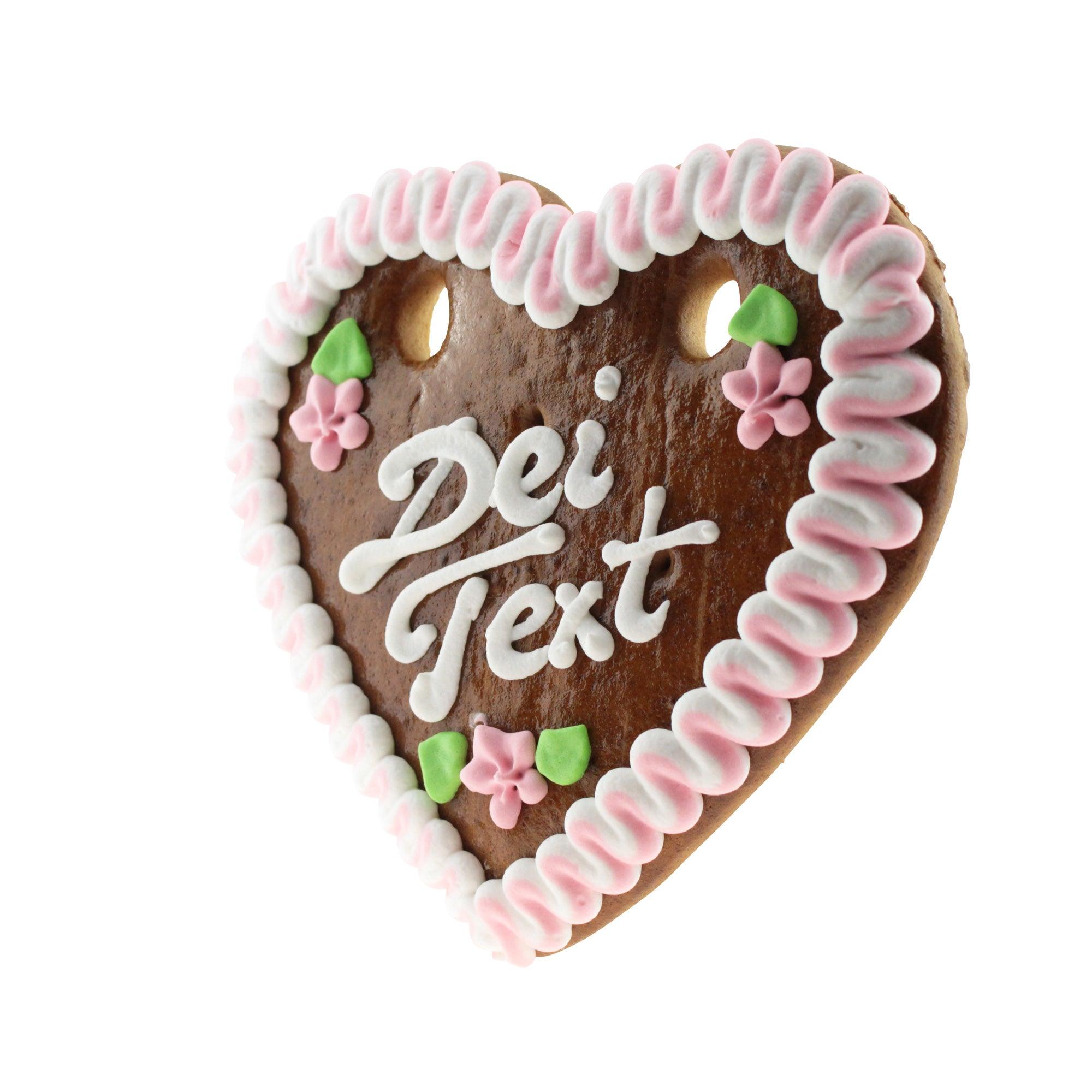 Braunes Lebkuchenherz mit weißer und rosa Zuckerdekoration, rosafarbenem Rand und Wunschtext in weißer Schrift.