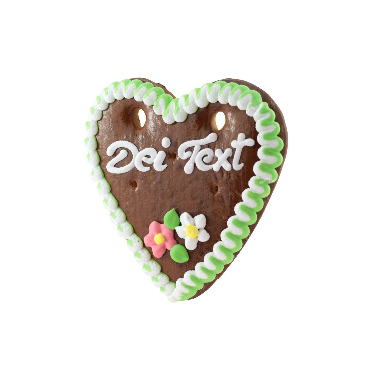 Herzförmiges Lebkuchen mit weißer Zuckerschrift, Rand aus rosa Zuckerguss, Blumendekor, individuell beschriftbar.