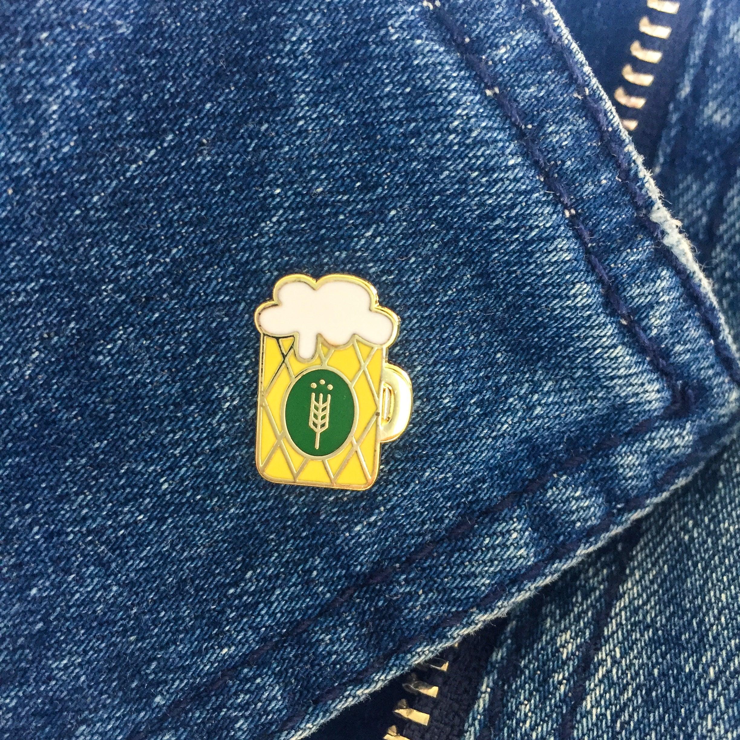 Pin in Form eines klassischen Bierkrugs mit weißem Schaum, gelbem Körper und schwarzem Umriss aus Hartemaille, ca. 1,3 x 1,8 cm.