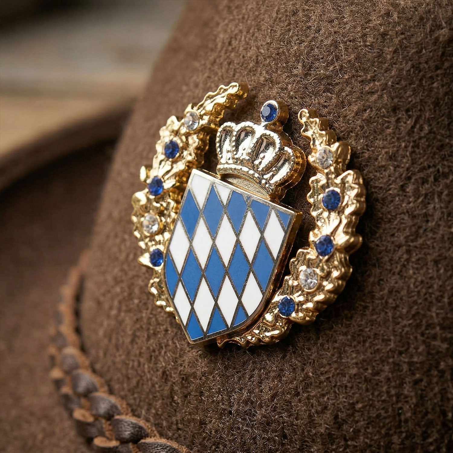 Goldfarbener Wappen Pin mit bayerischem Rautenmuster, Krone und blau-weißen Glassteinen auf braunem Filzhut