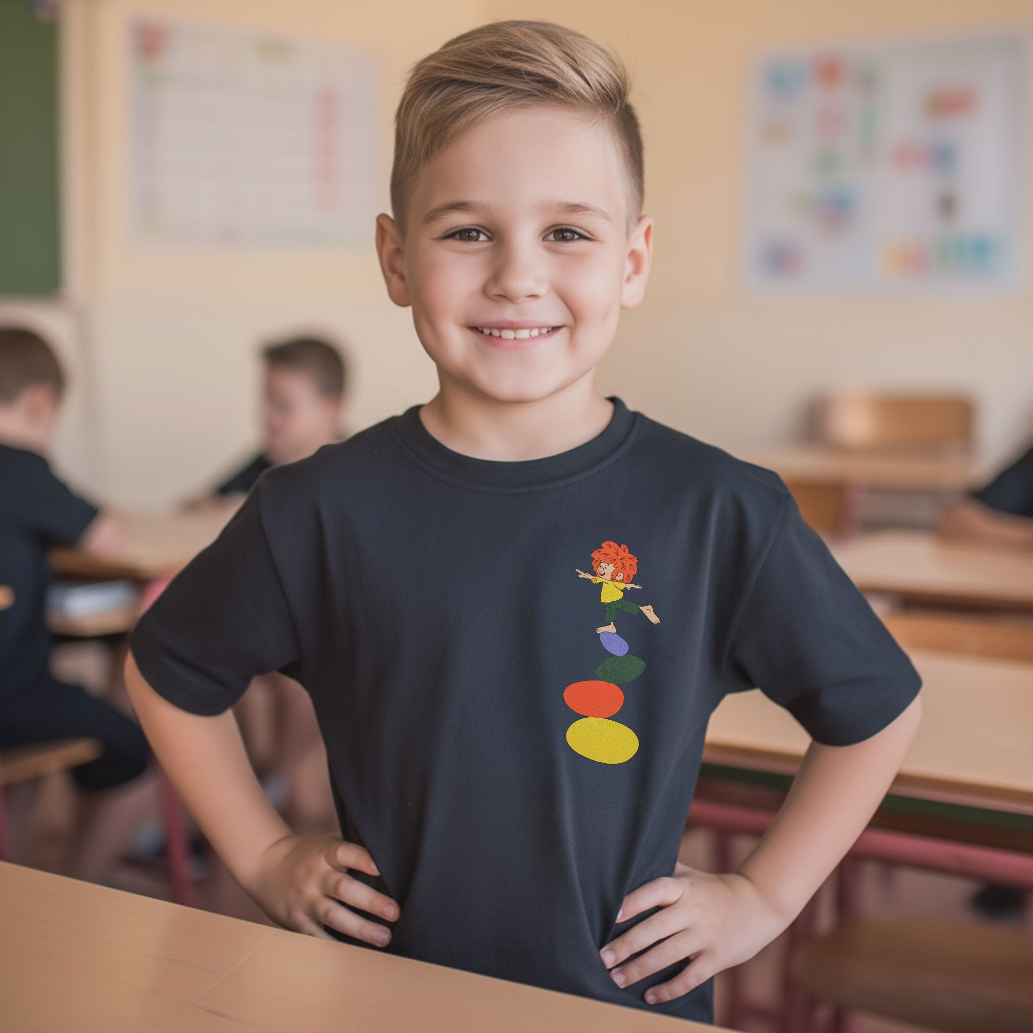 Glücklicher Junge in einem schwarzen Pumuckl Kinder T-Shirt Balance mit bunten Steinen im Klassenzimmer.
