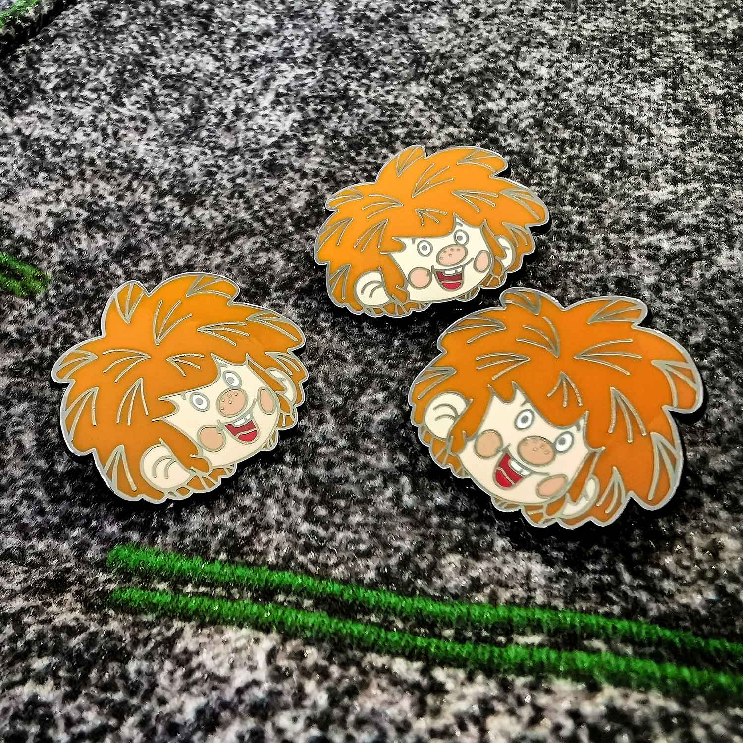 Drei Pumuckl Retro Cartoon Pins mit rotem Haar und lachendem Gesicht auf dunklem, strukturiertem Hintergrund.
