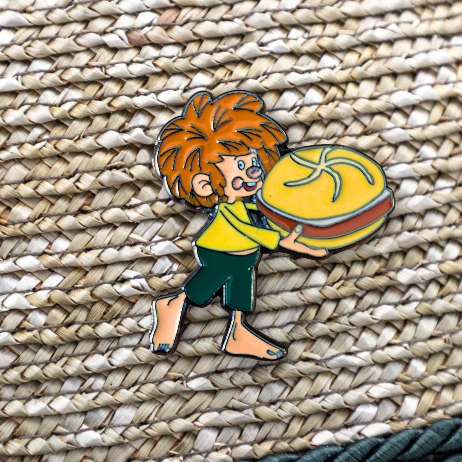 Pumuckl Pin mit rotem Haar und bayerischer Leberkassemmel auf geflochtenem Untergrund