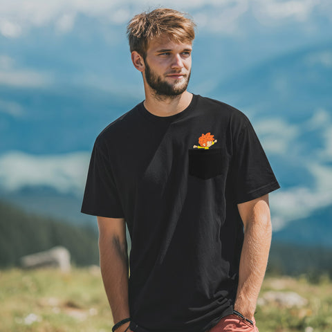 Mann im schwarzen Pumuckl T-Shirt „Nei da“ vor Bergkulisse, Pumuckl in der Brusttasche