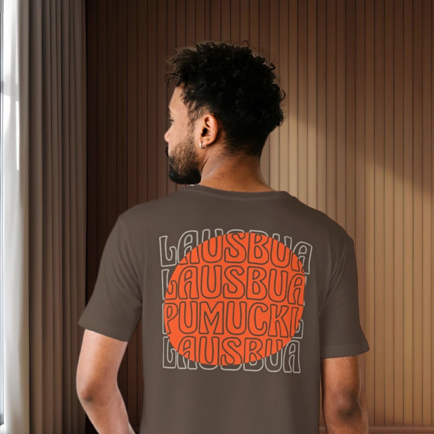 ®Pumuckl Herren T-Shirt "Lausbua" auf dem Rücken eines Mannes, orange Schrift auf braunem Stoff.