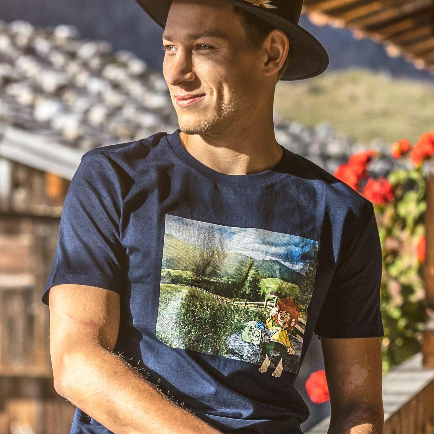 Mann trägt schwarzes ®Pumuckl Herren T-Shirt "Berg-Kobold" mit Koboldmotiv und Alpenlandschaft.