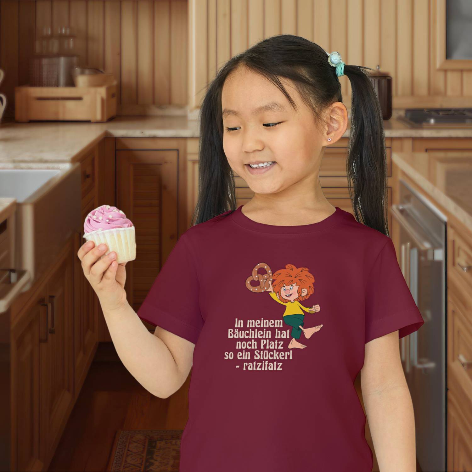 Lachendes Kind in bordeauxrotem Pumuckl Kinder T-Shirt Brezn Stückerl mit Brezel-Motiv und Spruch.