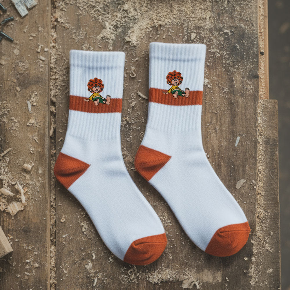 Zwei weiße Pumuckl Tennissocken mit orangefarbenen Streifen und Saum, auf Holzuntergrund drapiert.