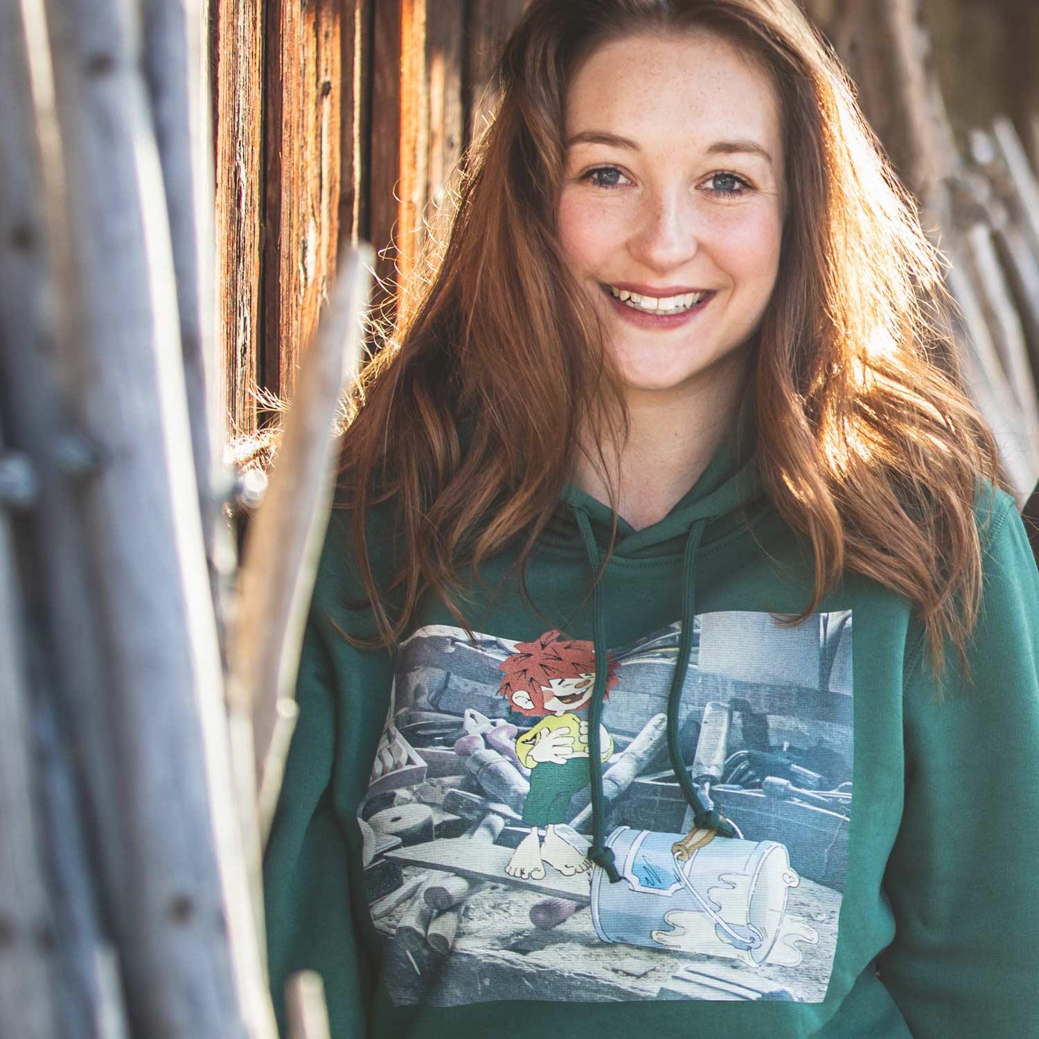 Damen-Kapuzenpullover mit Frontprint „Werkstatt“ und Pumuckl-Motiv, aus Bio-Baumwolle und recyceltem Polyester.