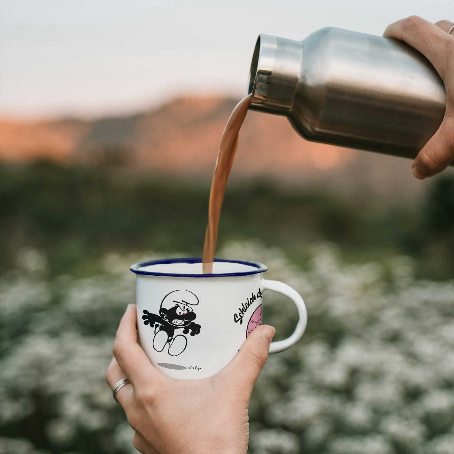 Schlümpfe Emailletasse Schleich di mit bösem Schlumpf-Motiv, in die ein Getränk aus einer Isolierflasche gegossen wird.