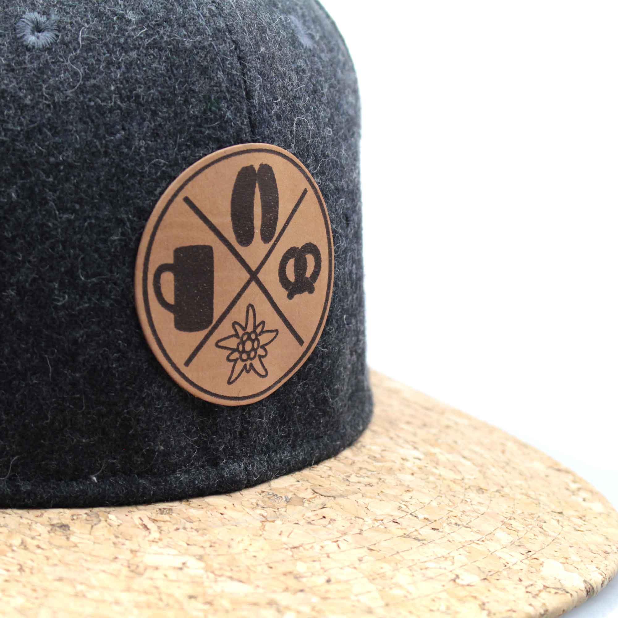 Graue Snapback Cap in Filzoptik mit flachem Korkschild und aufgenähtem Patch mit dem Schriftzug „Boarisch“.