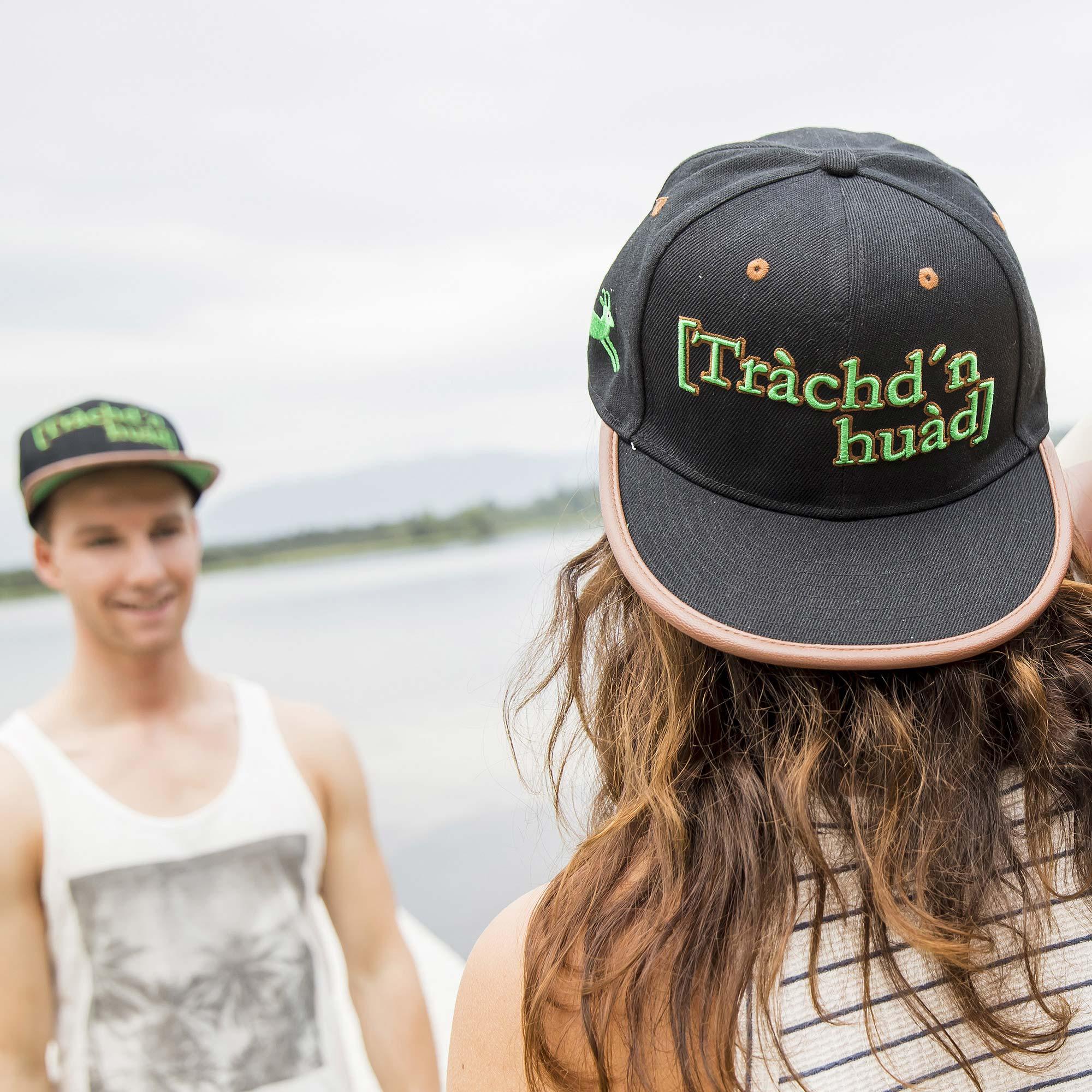 Frau mit schwarzem Snapback Cap "Tràchd'n huad" und Mann mit Cap im Hintergrund, am See.