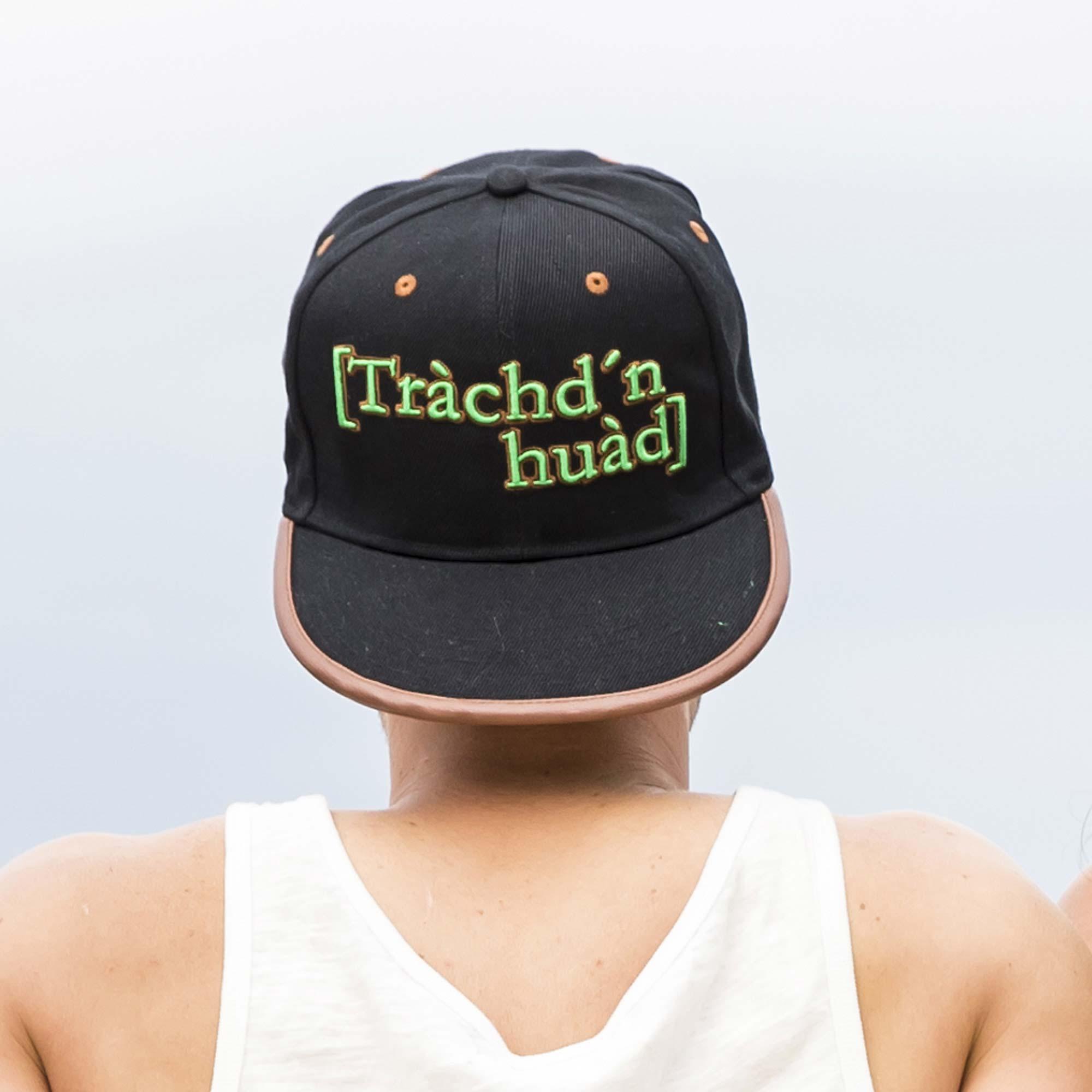 Person von hinten mit schwarzer Snapback-Cap und braunem Schirm, mit dem grünen Aufdruck "Trachd'n huad".