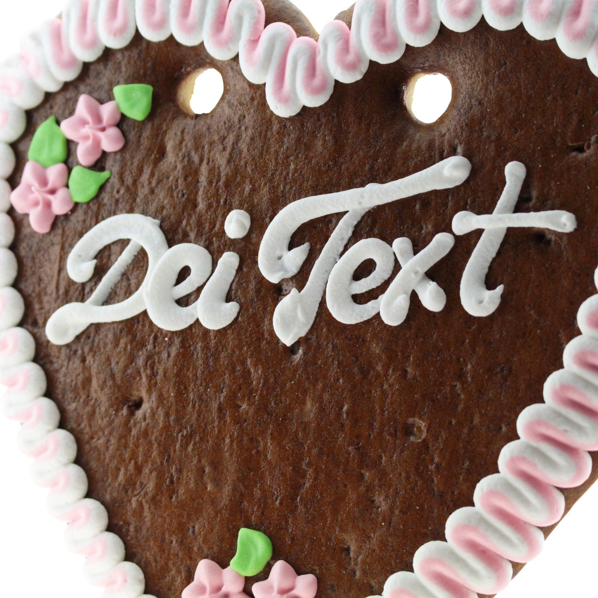 Braunes Lebkuchenherz mit weißem Rand, rosafarbenen Rosen, Zuckerdekor und individuell beschriftbarem Text. Ca. 22 × 23 cm.