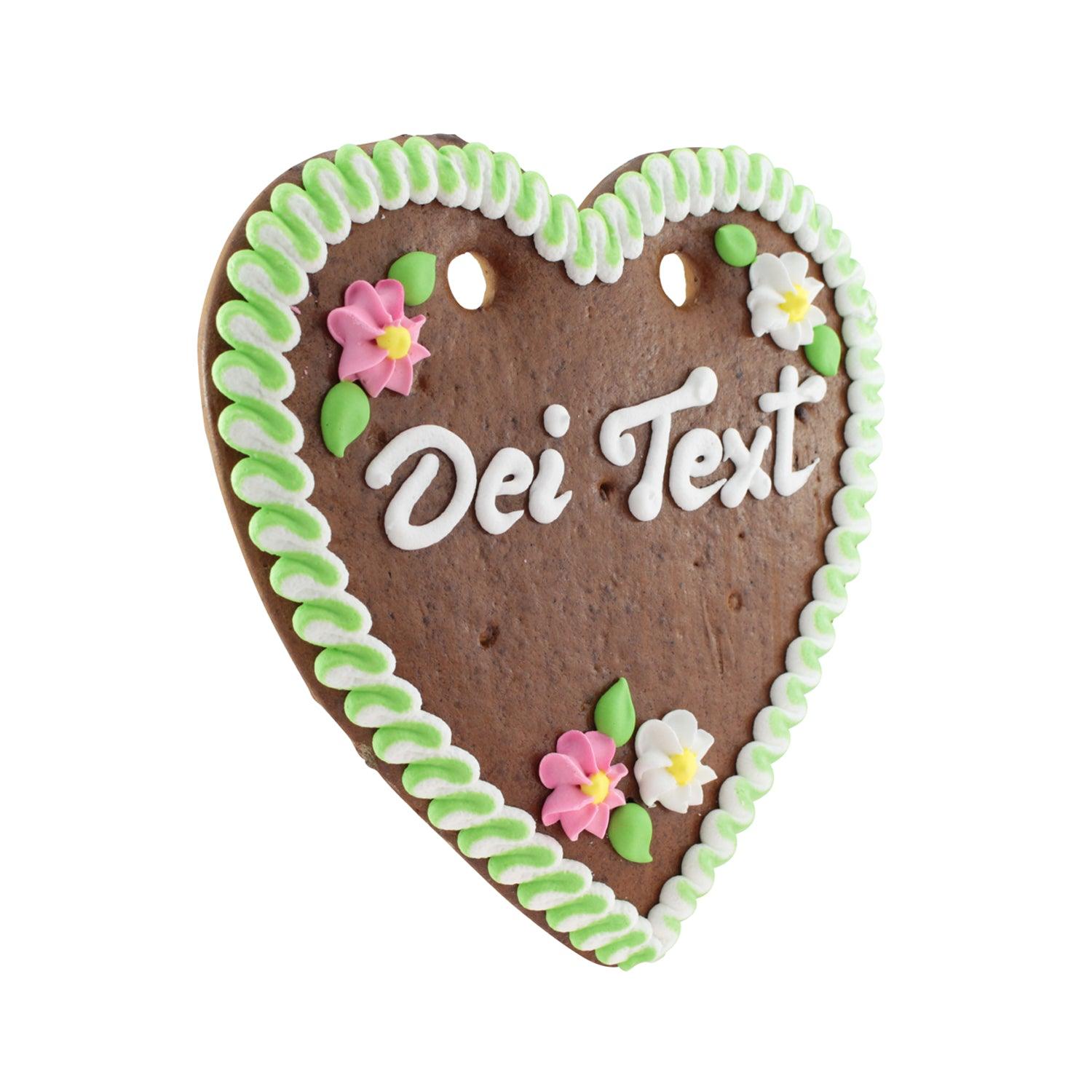 Herzförmiges Lebkuchen mit rosa Zuckerguss-Rand, Schriftzug in Weiß, verziert mit Blumen, ca. 22 x 23 cm.